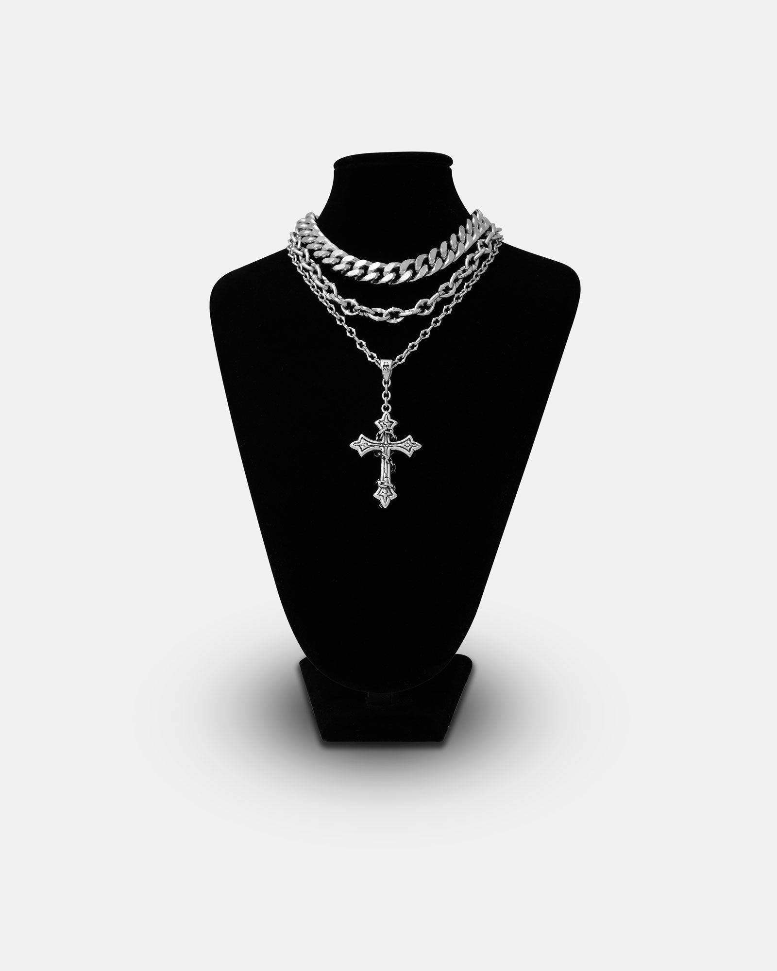 The Untouchable Stack features three layered silver chains—a chunky Cuban chain, a cathedral necklace, and a long chain with an ornate cross pendant—displayed on a black bust against a plain white background.