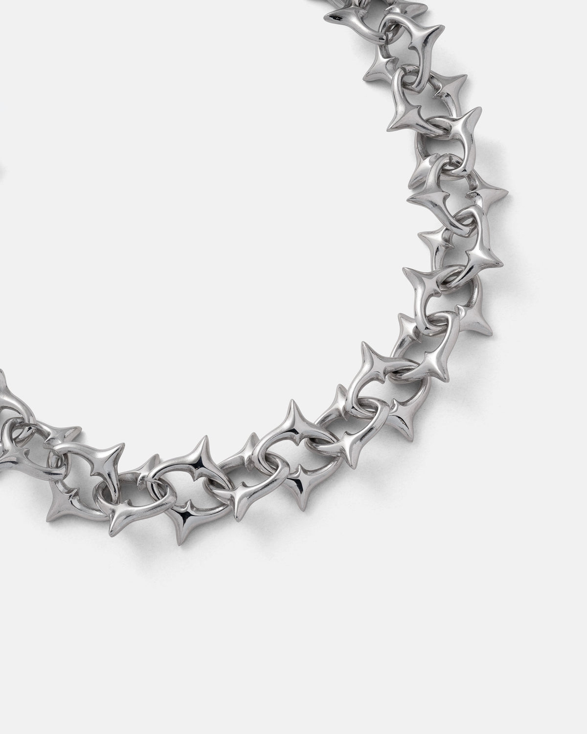 A close-up of Statement Collective’s "The Cathedral" XL 15mm Spiked Chain showcases its silver gothic design with interlocking star-shaped links, artfully arranged in a partial circle against a plain white background.