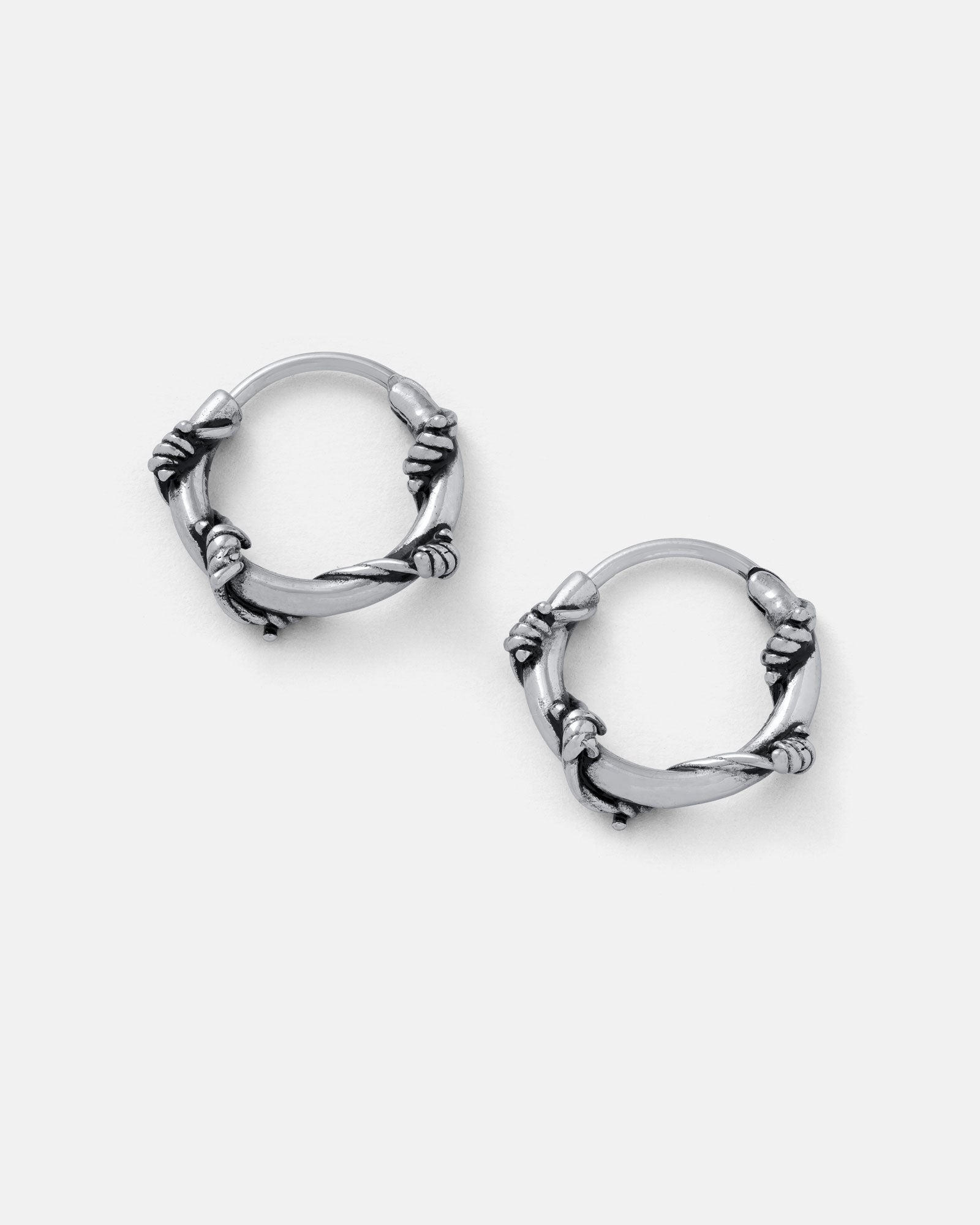The Barbed Wire Hoop Earrings, crafted from stainless steel to mimic intertwined wire, are shown on a plain light gray background.