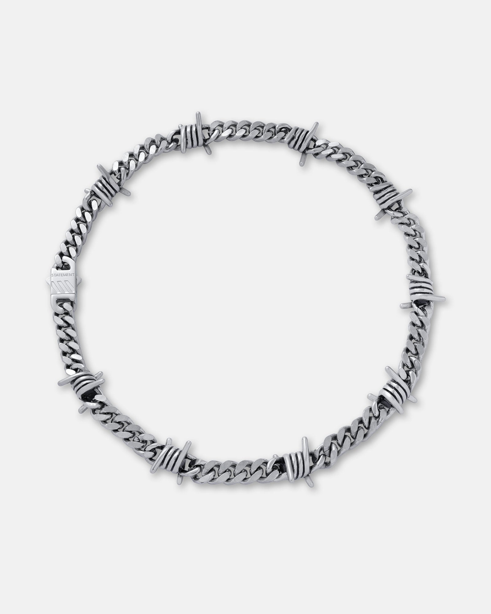 The 9mm Barbed Wire Cuban Chain features twisted silver barbed wire sections woven along a flat cuban link. Styled in a circle on a plain light background, this statement necklace stands out with its bold, unique design.