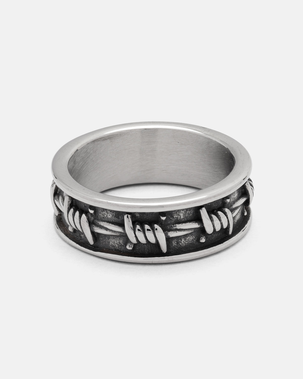 The Barbed Wire Ring by Statement Collective features a silver, twisted barbed wire design crafted from durable 316L stainless steel, with textured detailing and a darkened background for striking contrast, displayed on a plain white surface.