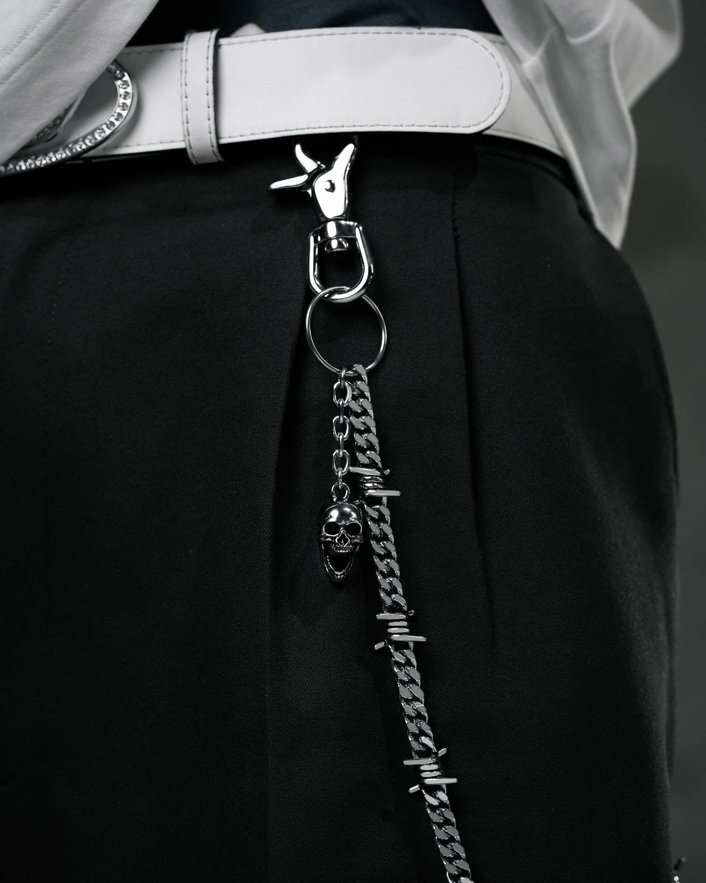 Close-up of a person wearing black pants and a white belt with the 9mm Barbed Wire Cuban Wallet Chain, featuring barbed wire-style links and a skull charm, clipped to a belt loop.