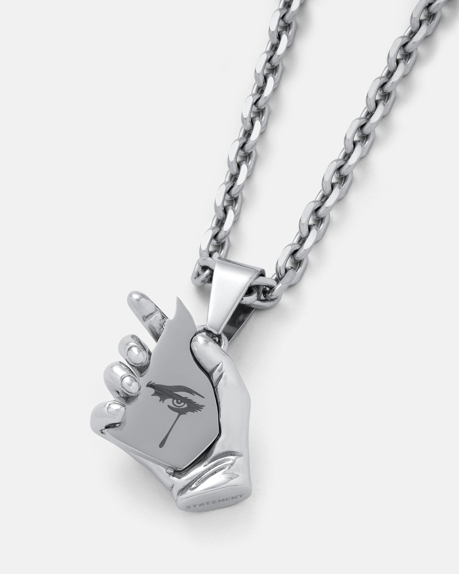The Broken Mirror" Pendant is a silver chain necklace with an avant-garde pendant shaped like a hand holding a mask, featuring a single eye and teardrop design.