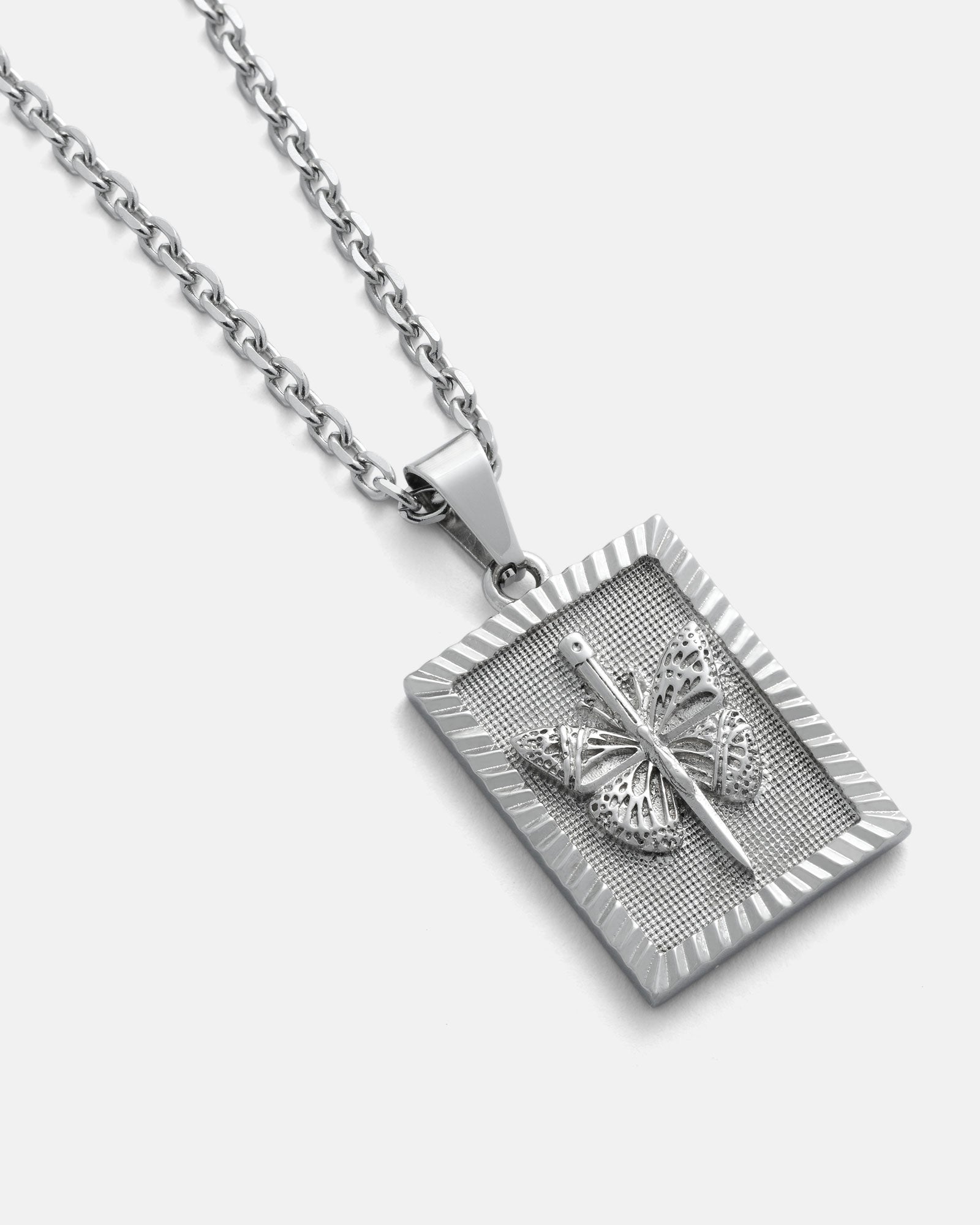 The Butterfly Tag Pendant is a silver necklace with a rectangular butterfly pendant featuring detailed tattoo flash-inspired design, shown on a textured background against a plain white surface.