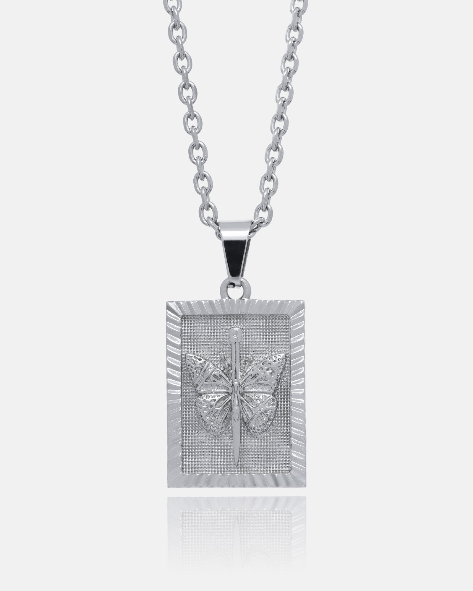 The Butterfly Tag Pendant is a silver necklace with a rectangular pendant inspired by tattoo flash, featuring a raised butterfly in the center and a textured border on a medium-width chain, shown against a white background.