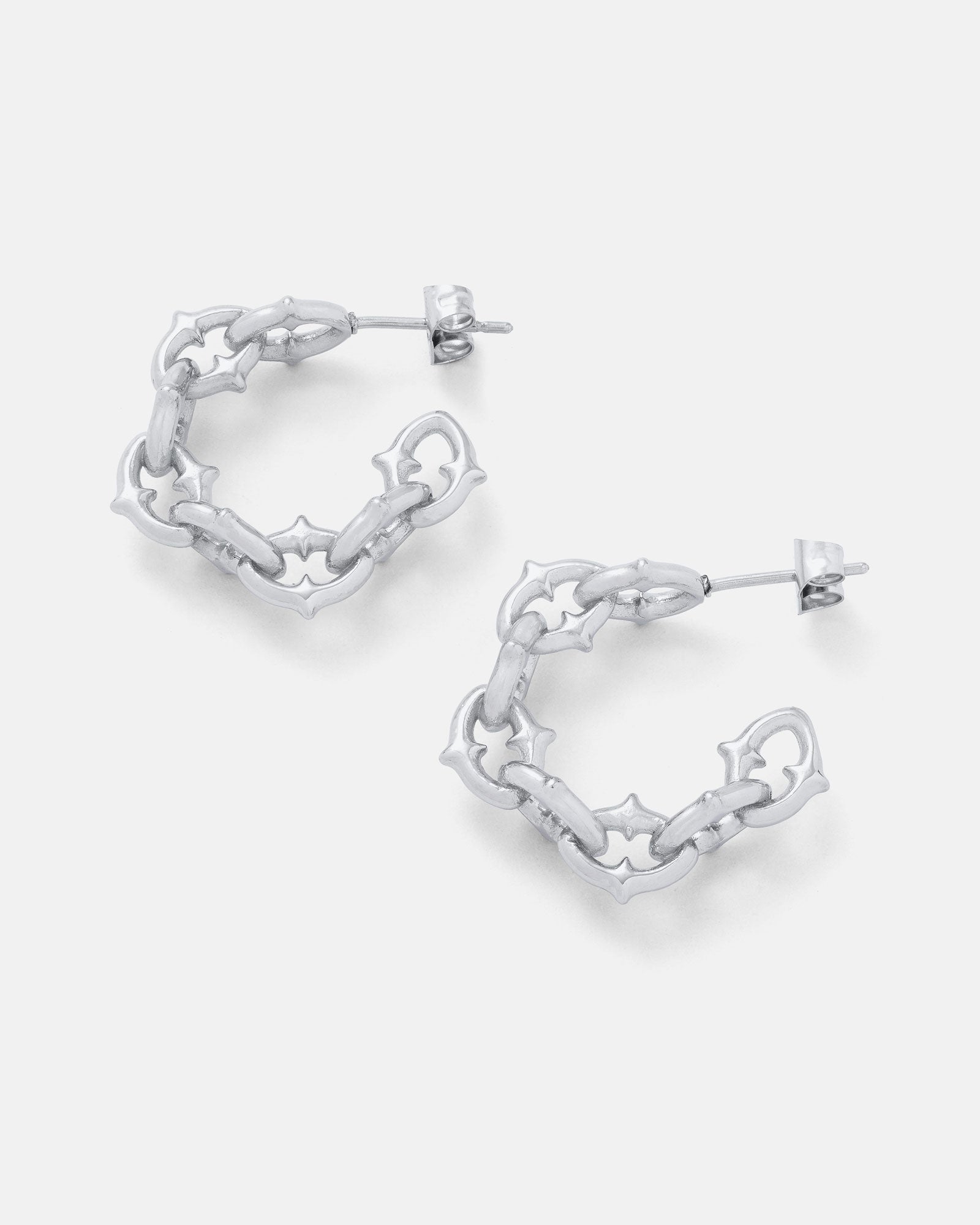 The Cathedral" Hoop Earrings feature a silver, chunky chain-link design with star-shaped cutouts—perfect for adding a gothic-inspired edge to any look. Displayed on a light gray background.