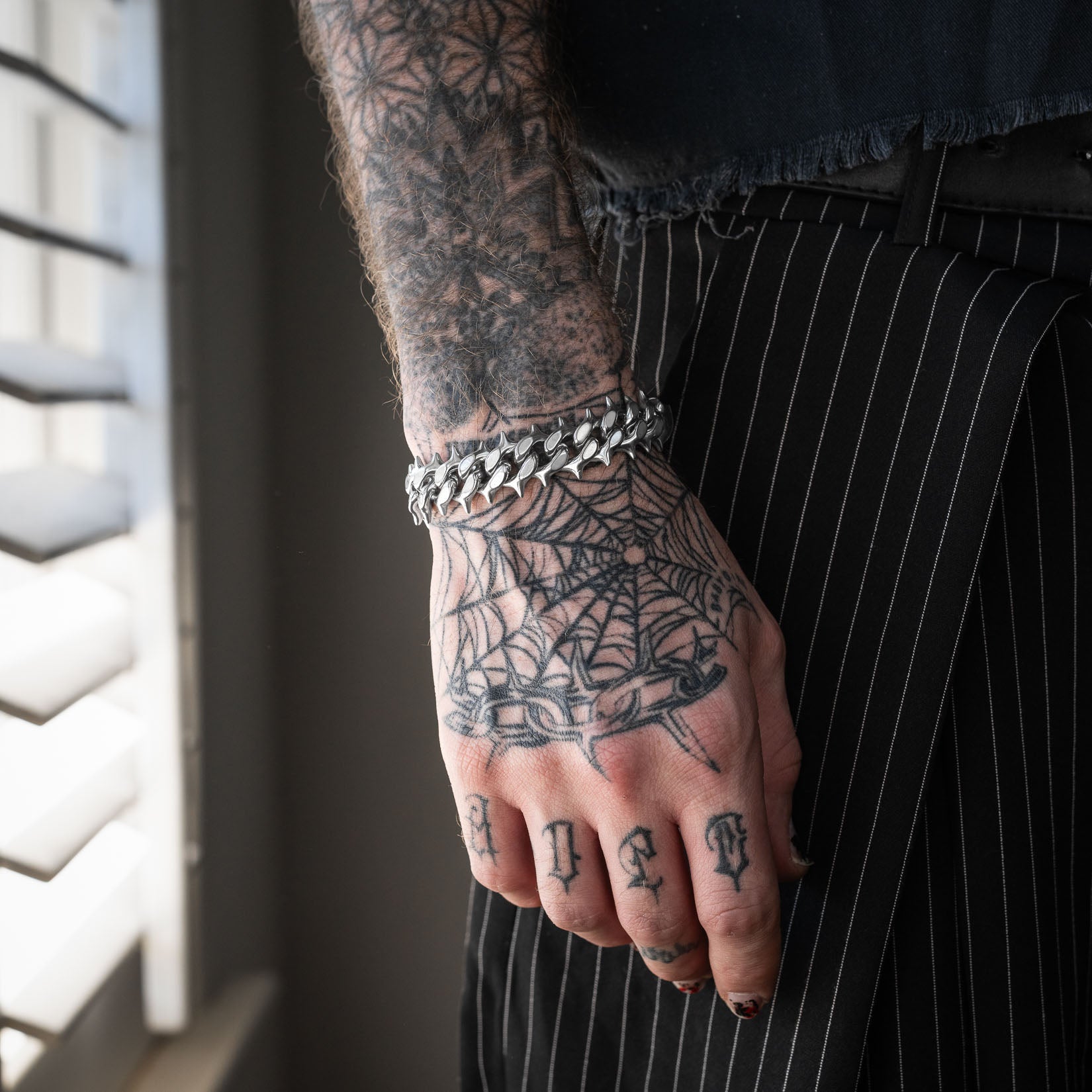 Tattooed men's hand wearing cuban bracelet with spiked links by statement collective