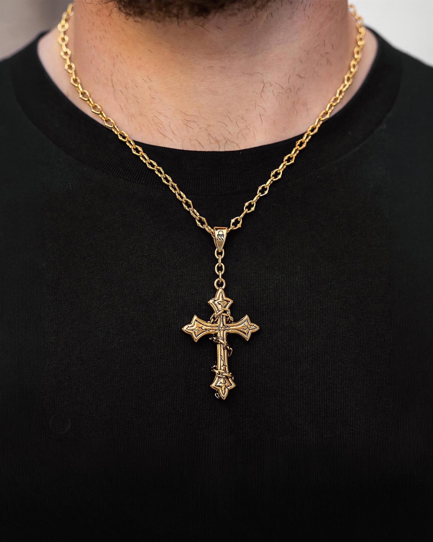 A person wears Statement Collective's "The Cathedral" 6mm Spiked Chain with a custom pendant (Gold) over a black shirt. The detailed cross pendant sits centered on the chest, adding sophisticated style to the look.