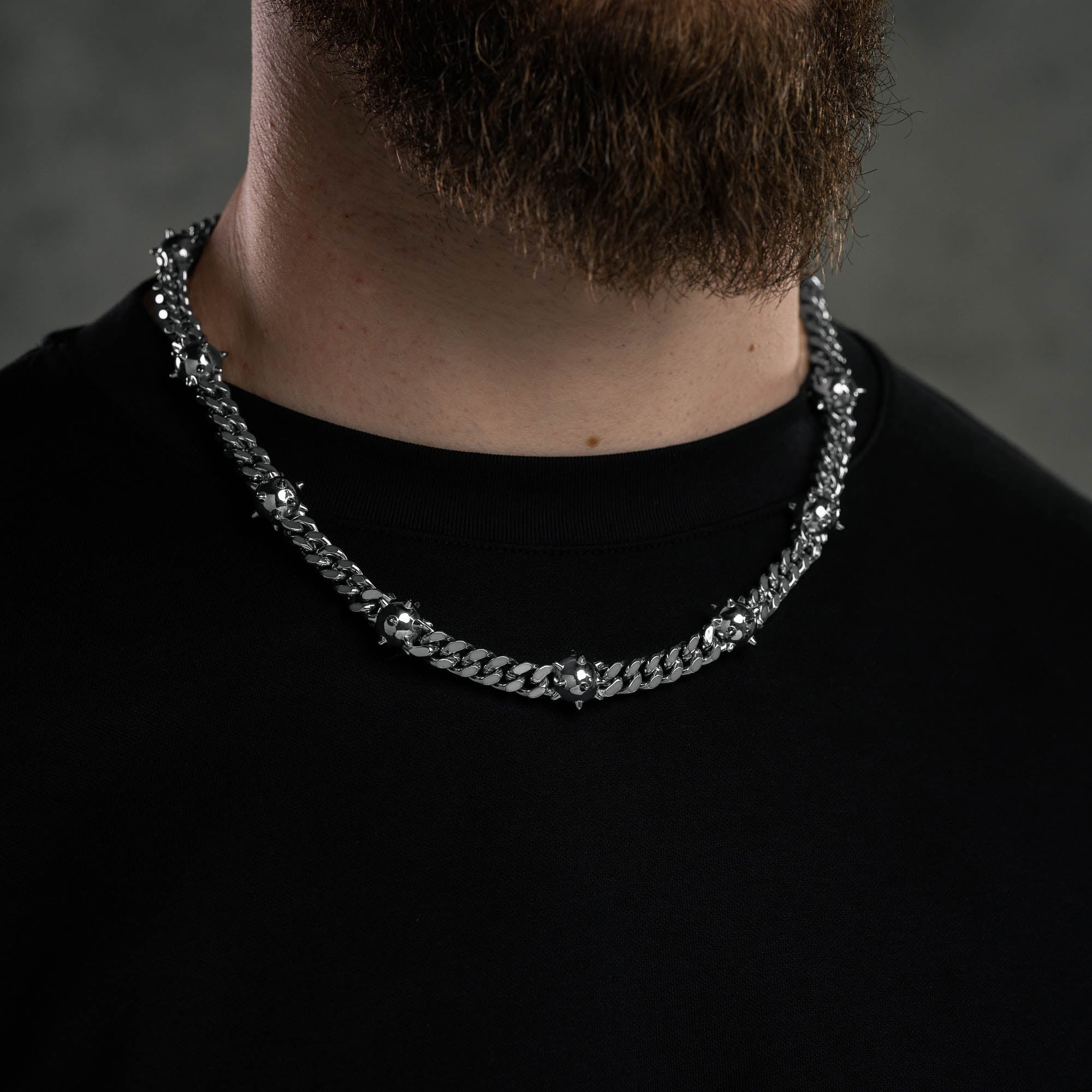 Man with beard wearing spiked ball cuban necklace against dark cement background