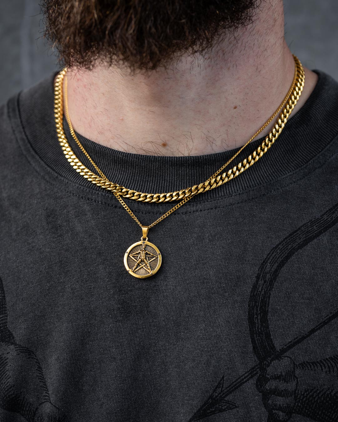 A close-up shows a person in a dark abstract T-shirt wearing the Statement Collective Cuban Set (Custom Pendant Choice) in gold; the bottom of their beard is visible.