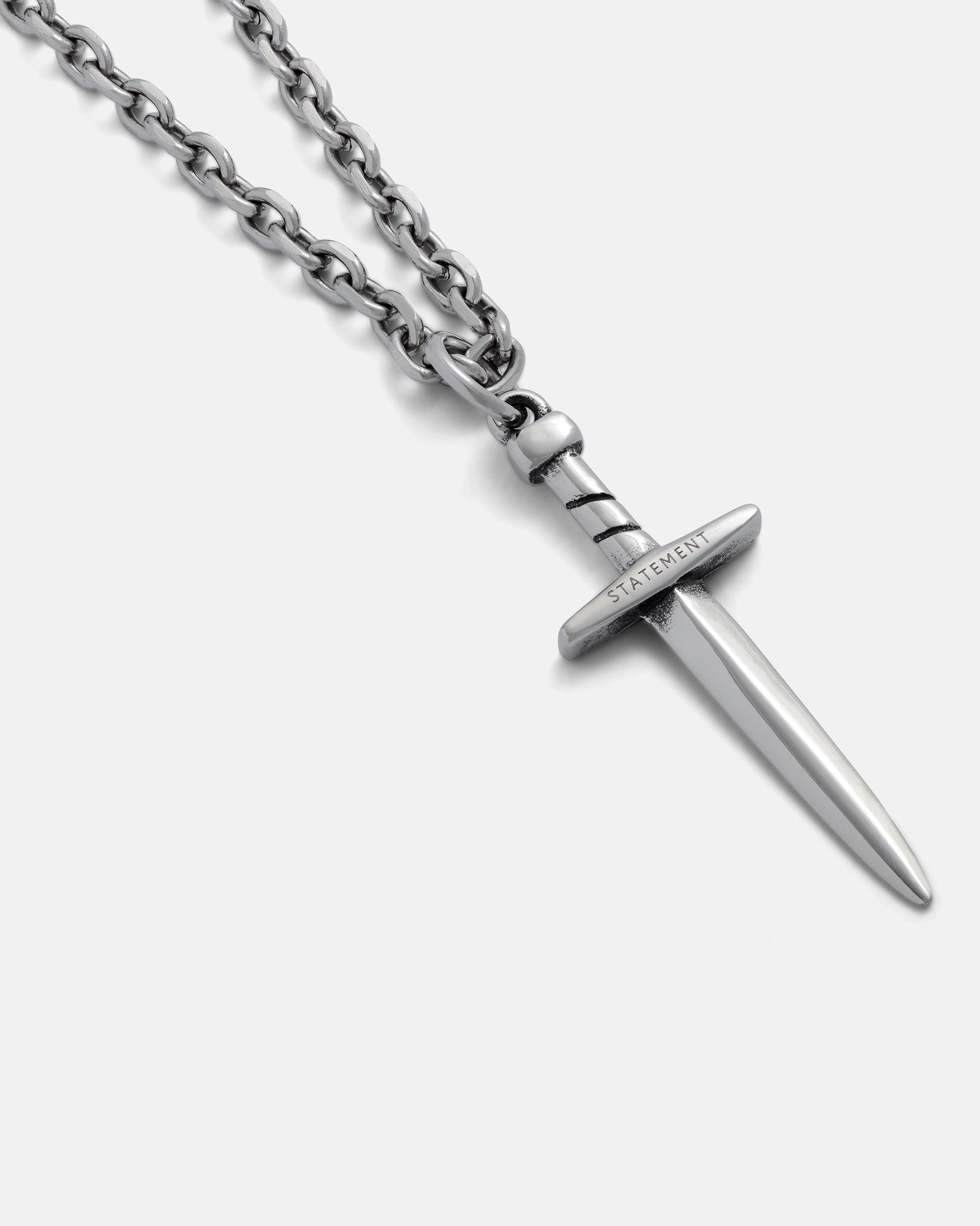 The Dagger Pendant is a silver chain necklace with an engraved "STATEMENT" hilt, shown on a light gray background—ideal for fans of hand-carved jewelry.