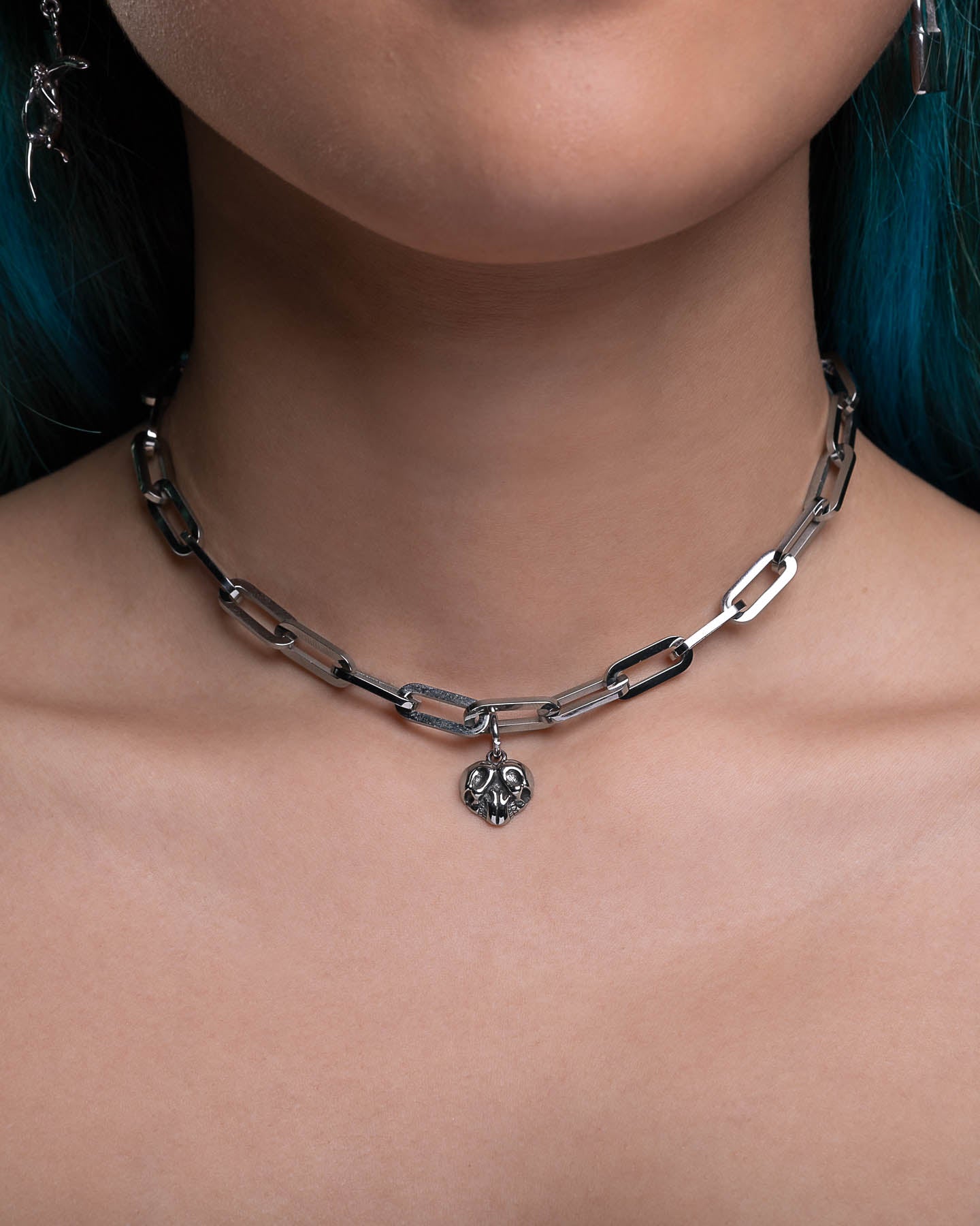 A close-up of a person’s neck showcases The Dainty Charm Choker (Custom Pendant Choice), featuring a chunky silver paperclip chain with a small heart-shaped pendant, set against a neutral background for emphasis.