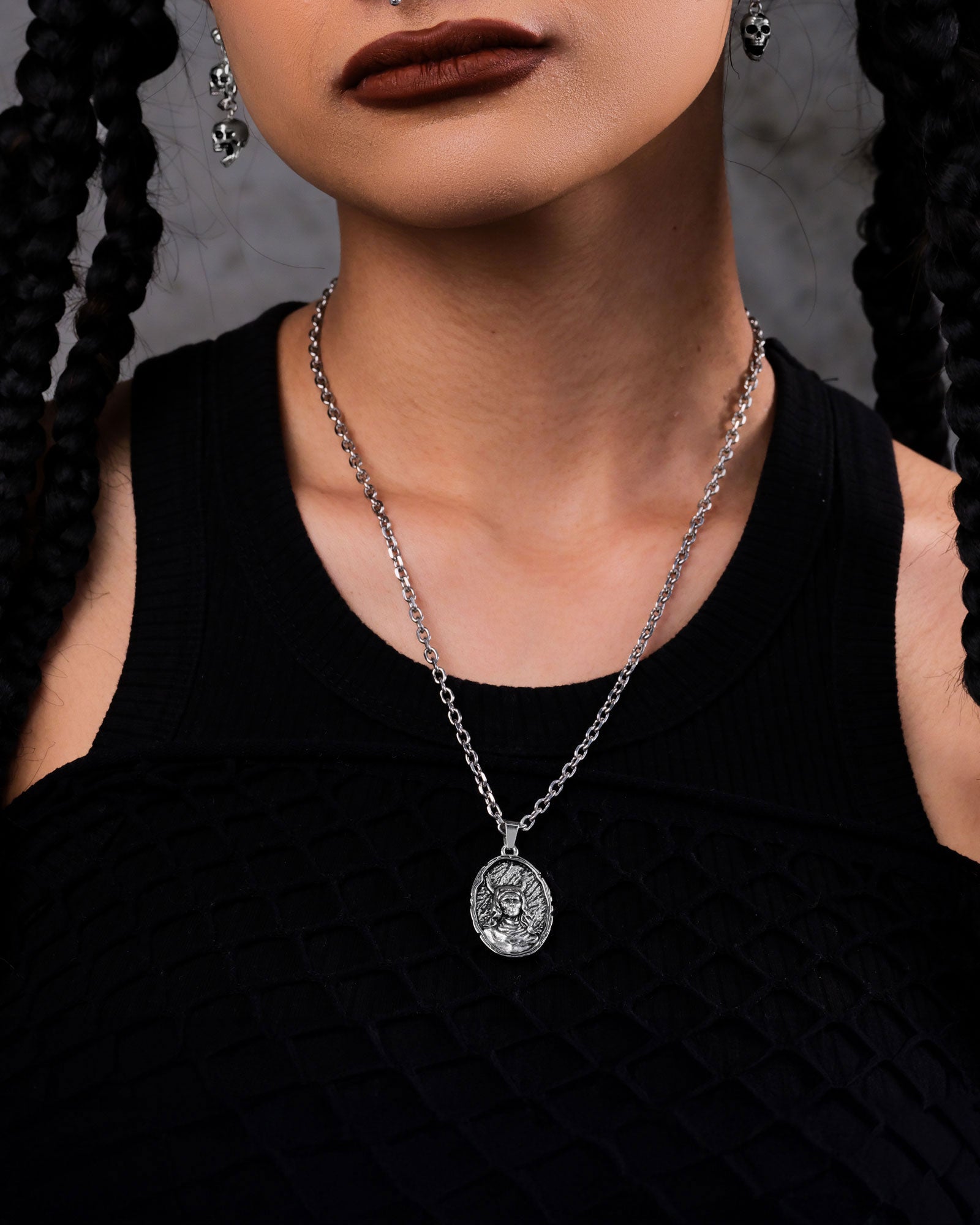 A person with braided hair, dark lipstick, a black textured top, and a silver chain with "The Unholy" Pendant—striking gothic jewelry—shows only the lower half of their face and neck.