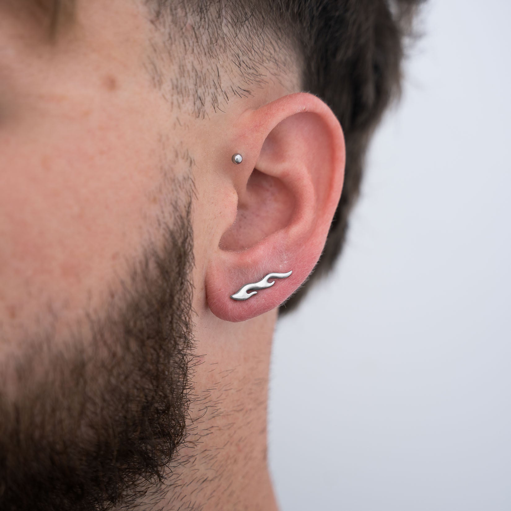 Close-up of a man's left ear with a silver flame earring on a plain background