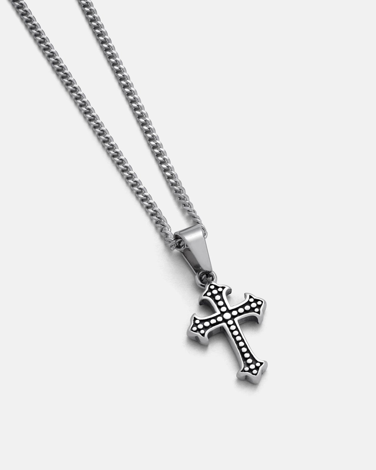 The Statement Collective French Cross Pendant, featuring dotted patterns, hangs from a sleek figaro chain and is displayed on a plain light grey background.