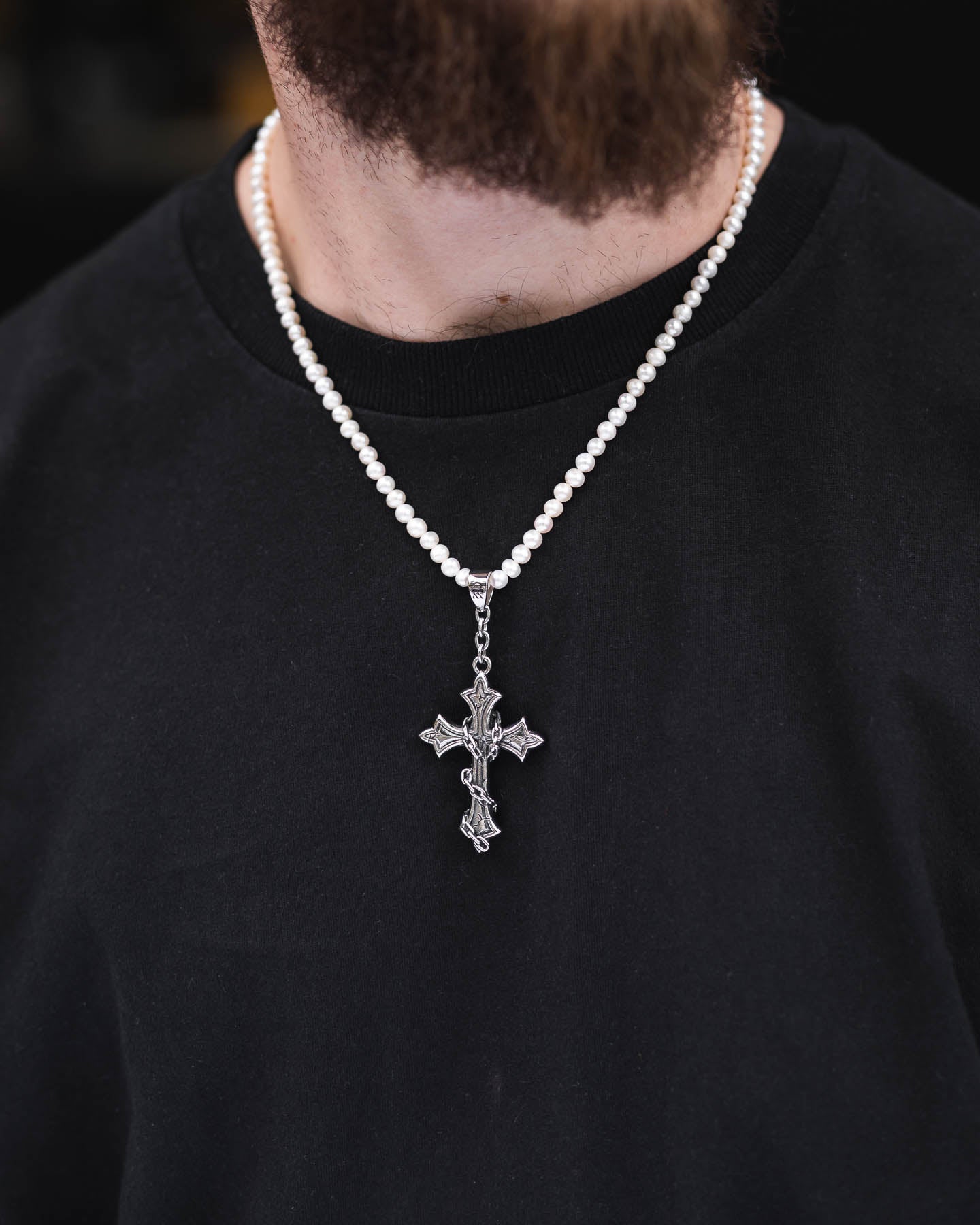 A person wearing a black shirt and the Freshwater Pearl Necklace With Custom Pendant Choice, featuring a silver crucifix pendant. Only the lower part of their face and neck is visible.