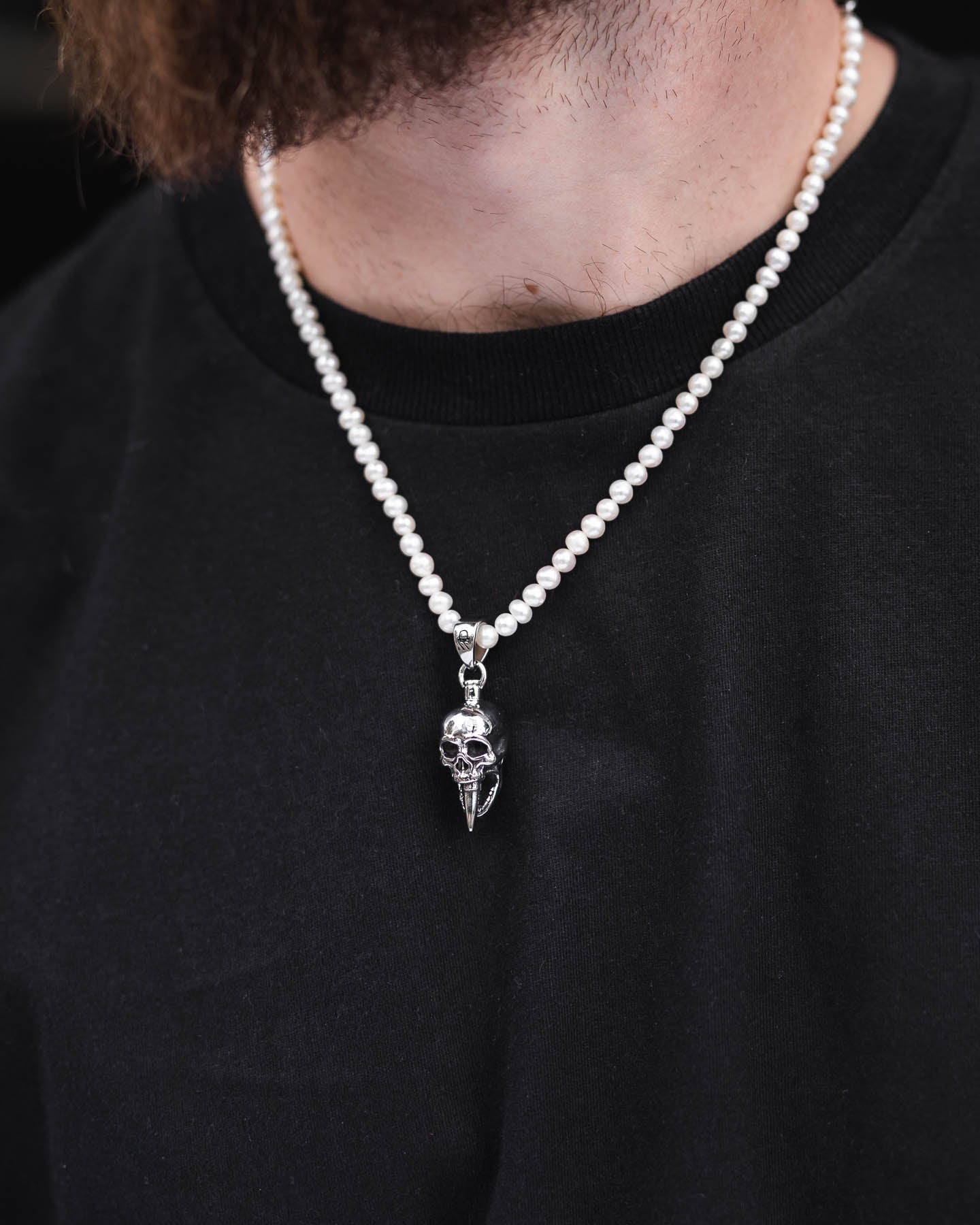 A person wears the Freshwater Pearl Necklace With Custom Pendant Choice featuring a silver skull pendant, shown on a black shirt with only the lower face, neck, and upper chest visible.