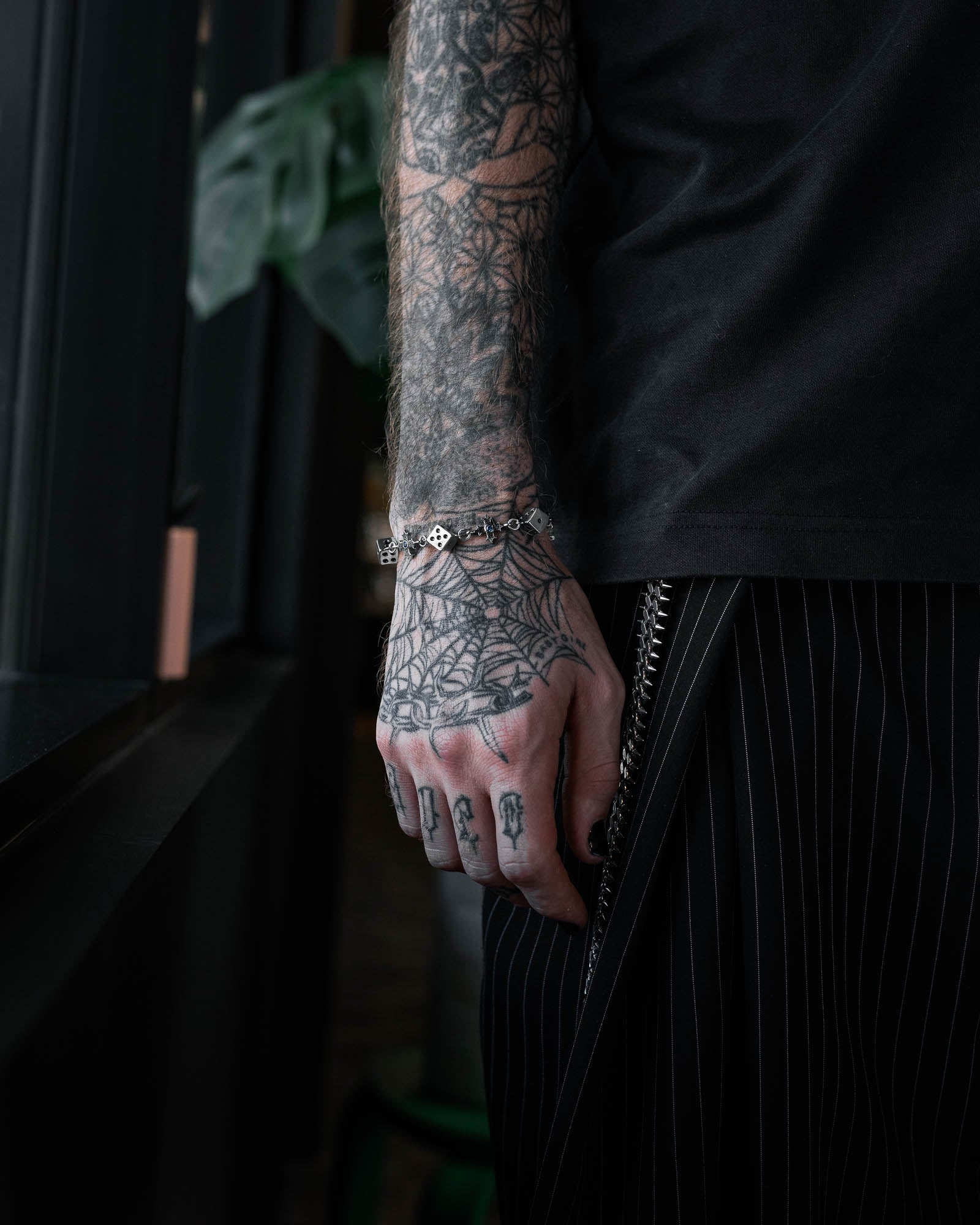 Person with tattooed arm wearing a steel bracelet of dice links and crosses by statement collective in a dark room