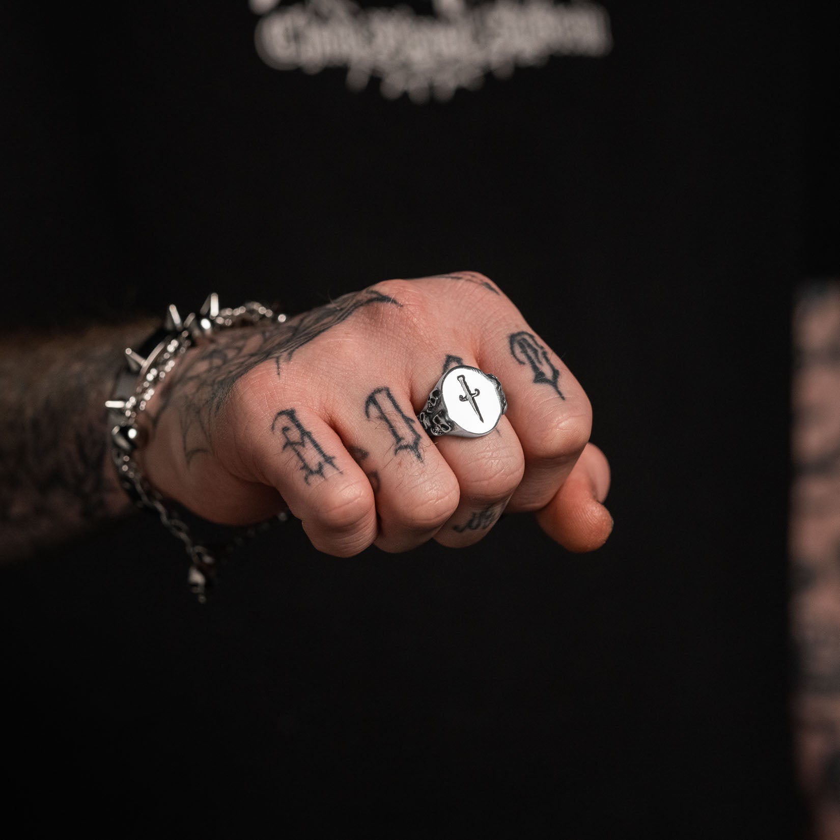 Hand with a silver signet ring  with dagger design on a black background