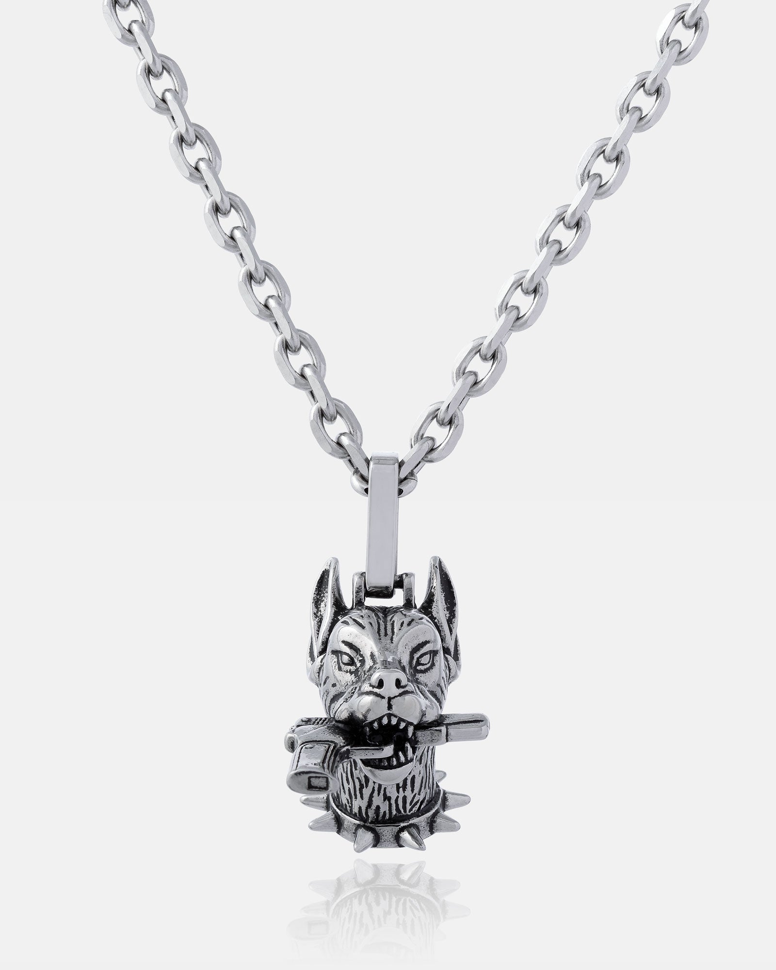 The Guard Dog" Pendant is a silver chain necklace with a detailed wolf’s head holding a small hammer and accented by a spiked collar—ideal for fans of bold hip hop jewelry.