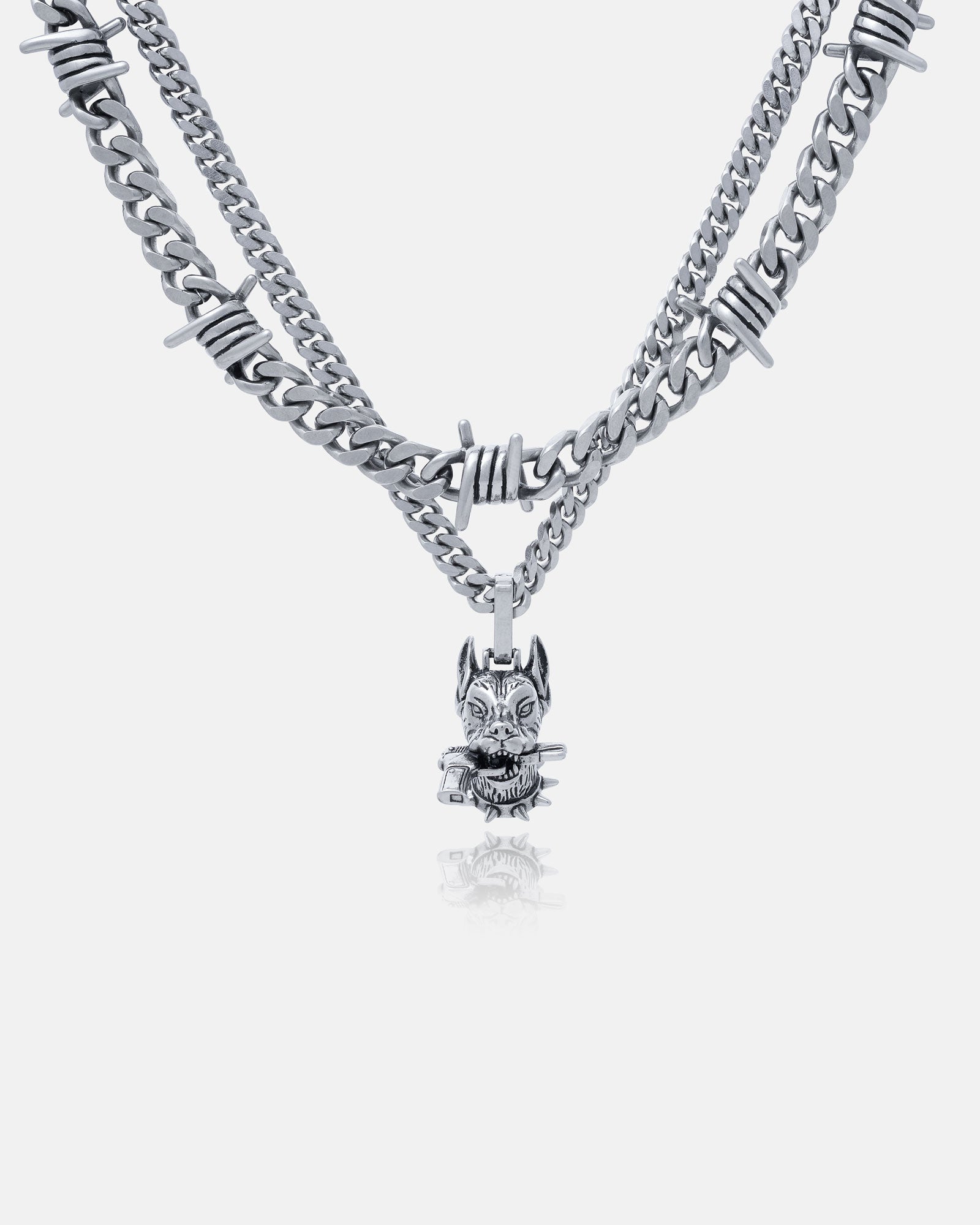 The Guard Dog" Set is a layered silver stainless steel chain necklace with barbed wire accents and a pendant shaped like a cat’s head and crossed bones, shown on a plain light background.