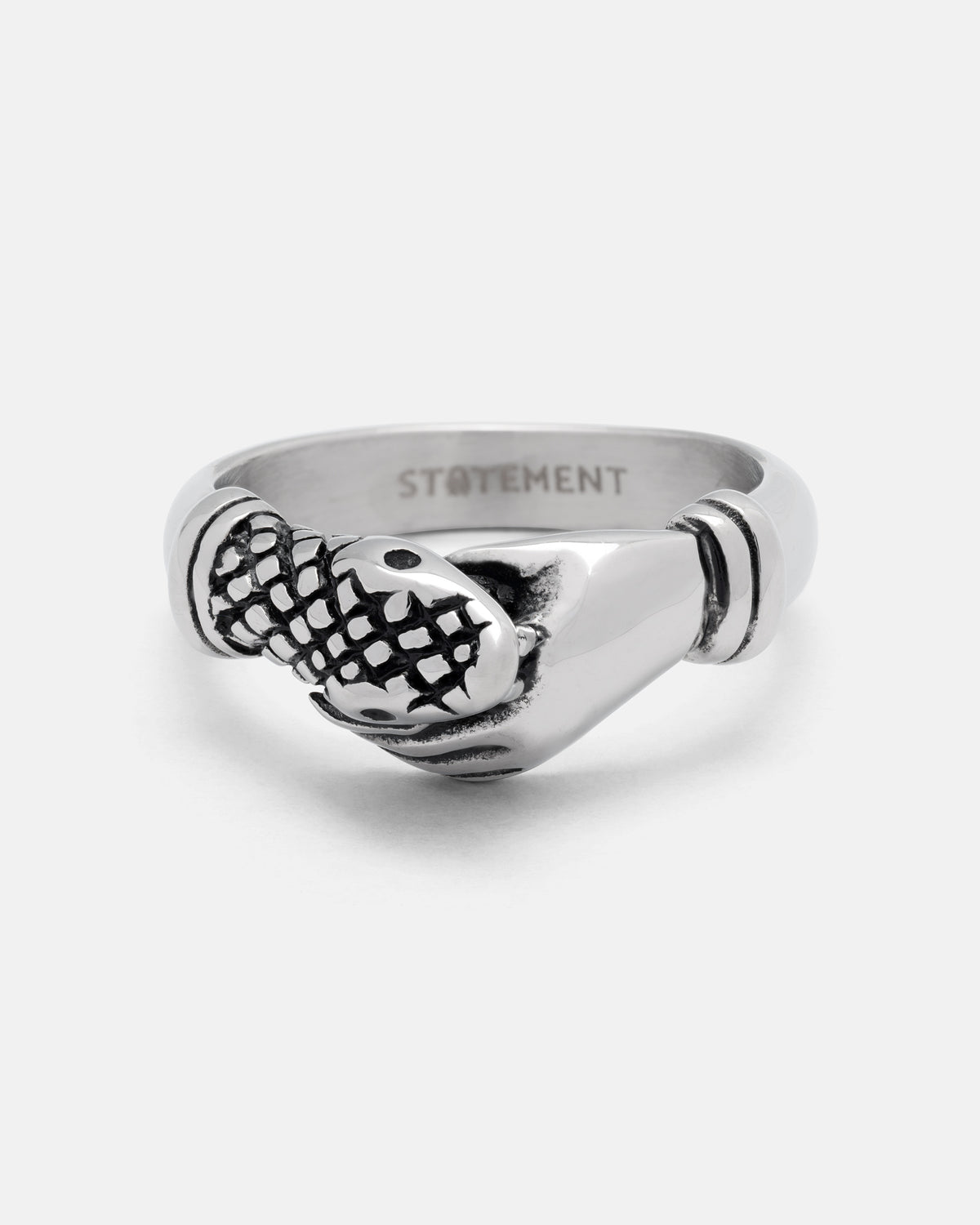 Introducing “The Hand That Bites” Ring by Statement Collective—a silver ring designed as a hand gripping a fish, highlighted by a subtle snakeskin pattern and engraved with STATEMENT inside the band.