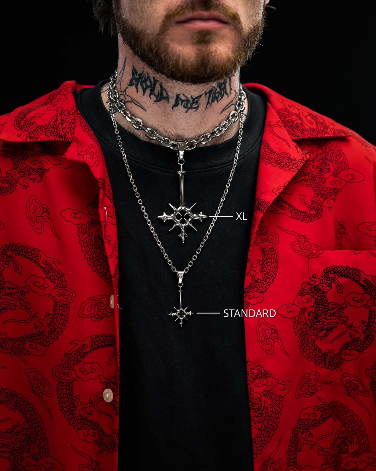 A person in a red patterned shirt and black t-shirt wears two silver necklaces from Statement Collective: the SAME X STATEMENT "Inversion" Pendant XL and the STANDARD version, each featuring a star-like RPG weapon-inspired pendant. Part of a neck tattoo is visible.