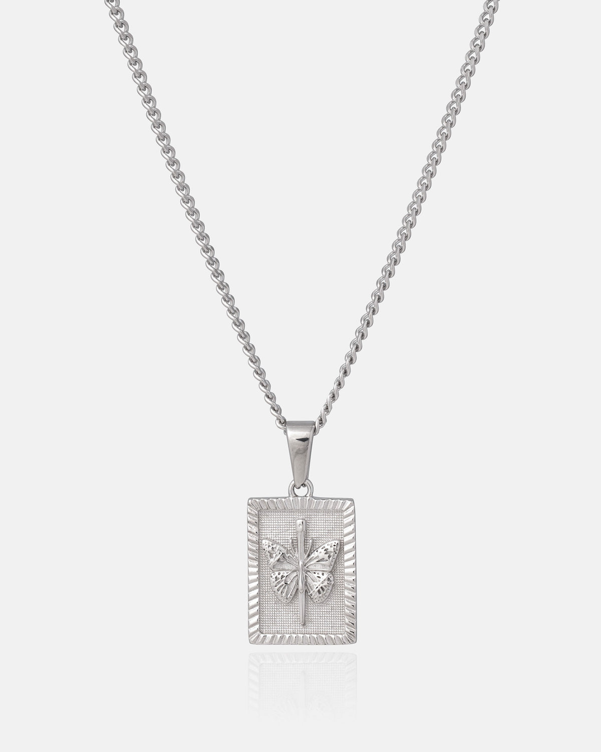The Mini Butterfly Tag Pendant by Statement Collective is a stainless steel silver chain necklace featuring a rectangular pendant engraved with a butterfly design on a textured background, photographed against a plain white surface. This piece subtly channels the allure of dark romance necklaces.