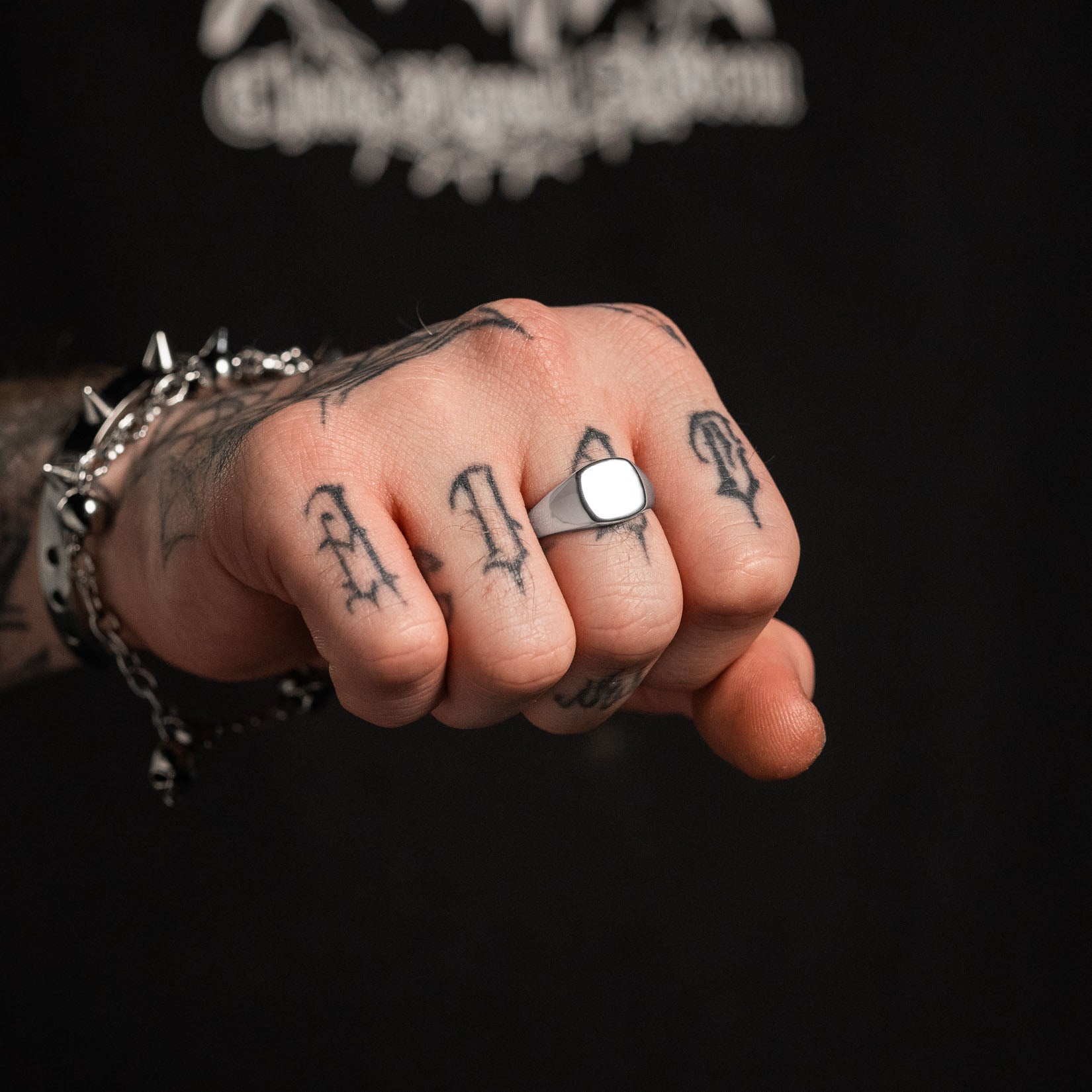 Hand with tattoos wearing a silver ring on a black background