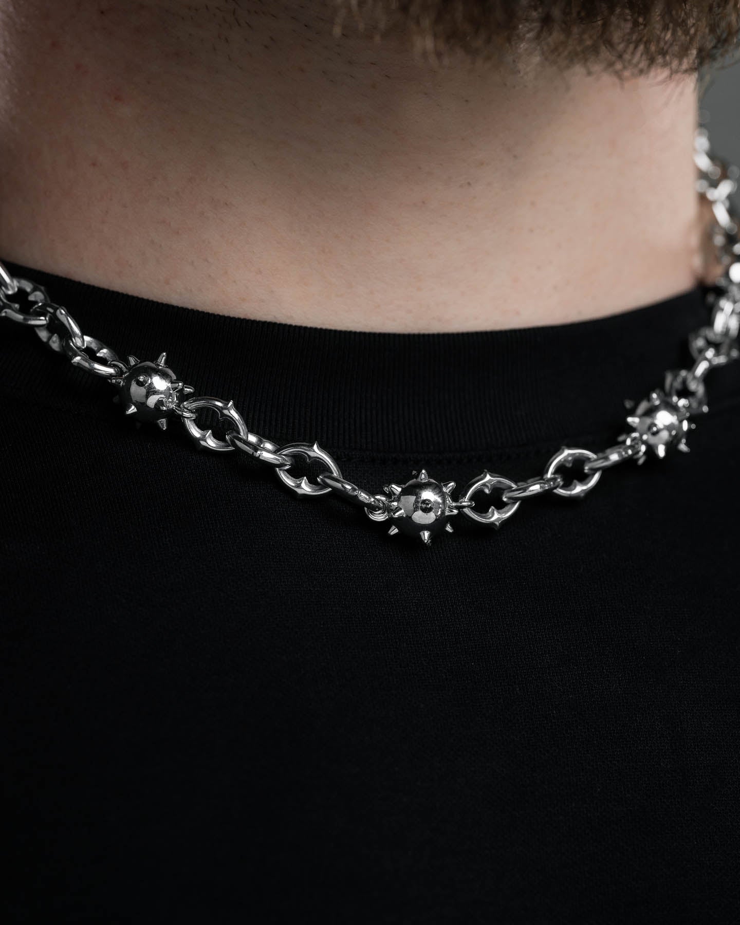 A close-up of a person wearing the "Morning Star" Cathedral Chain, a stainless steel necklace featuring spiked metal ball details, paired with a plain black shirt.