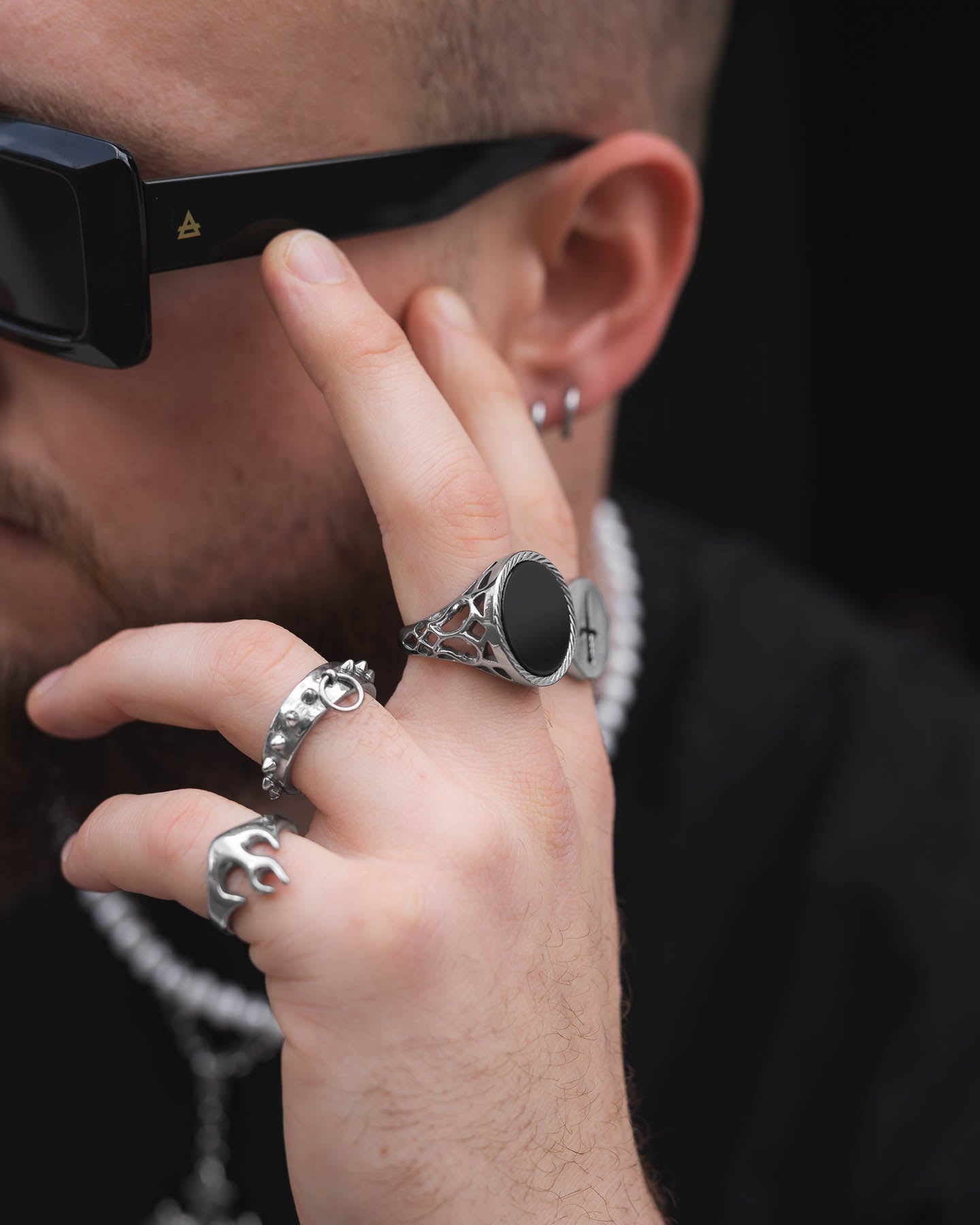 A person wearing dark sunglasses and a pearl necklace touches their face, highlighting the Onyx Sovereign Ring on their hand. The image focuses on the jewelry, especially the Onyx Sovereign Ring, against a blurred background.