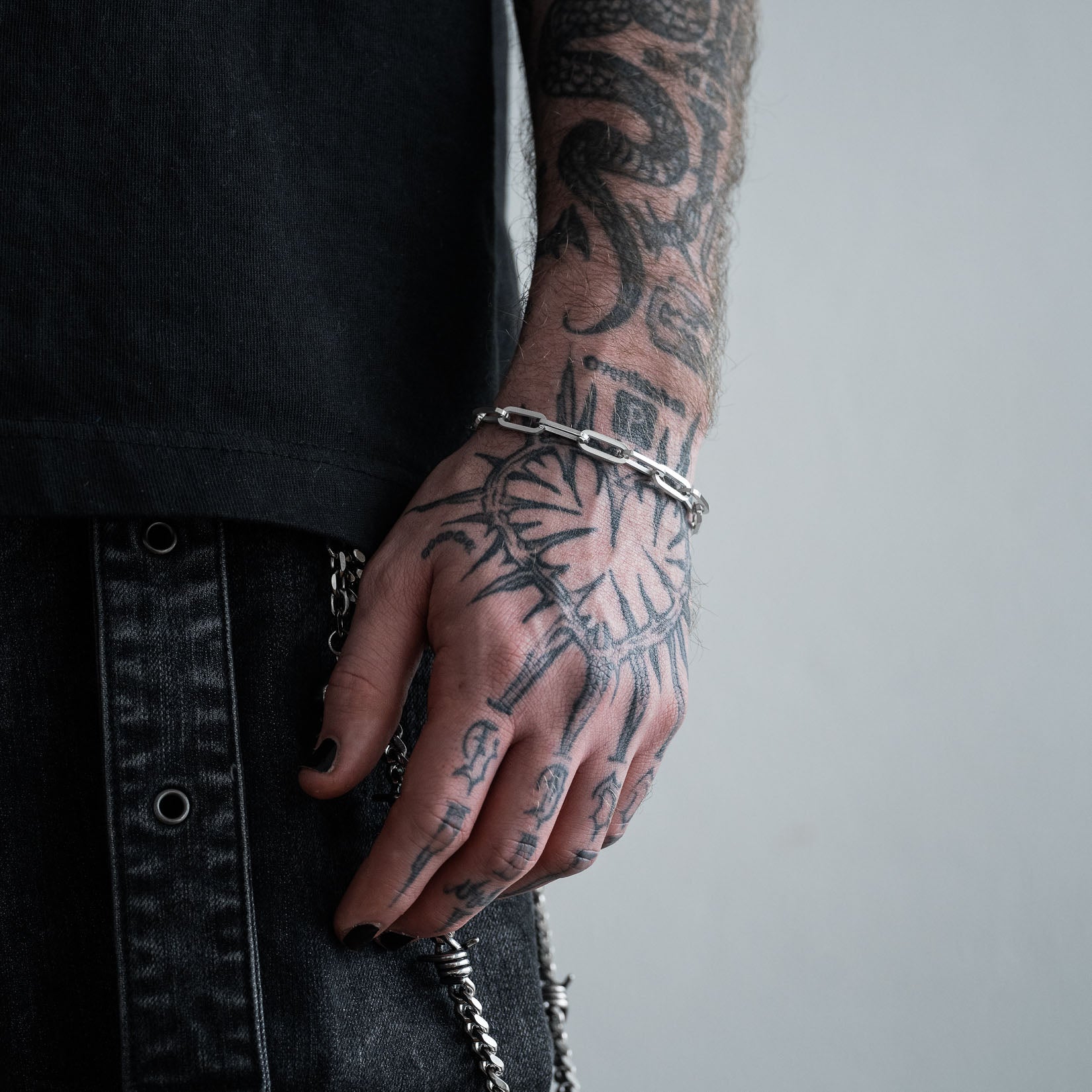 Person with tattooed hand wearing a 6mm silver paperclip bracelet on a plain background