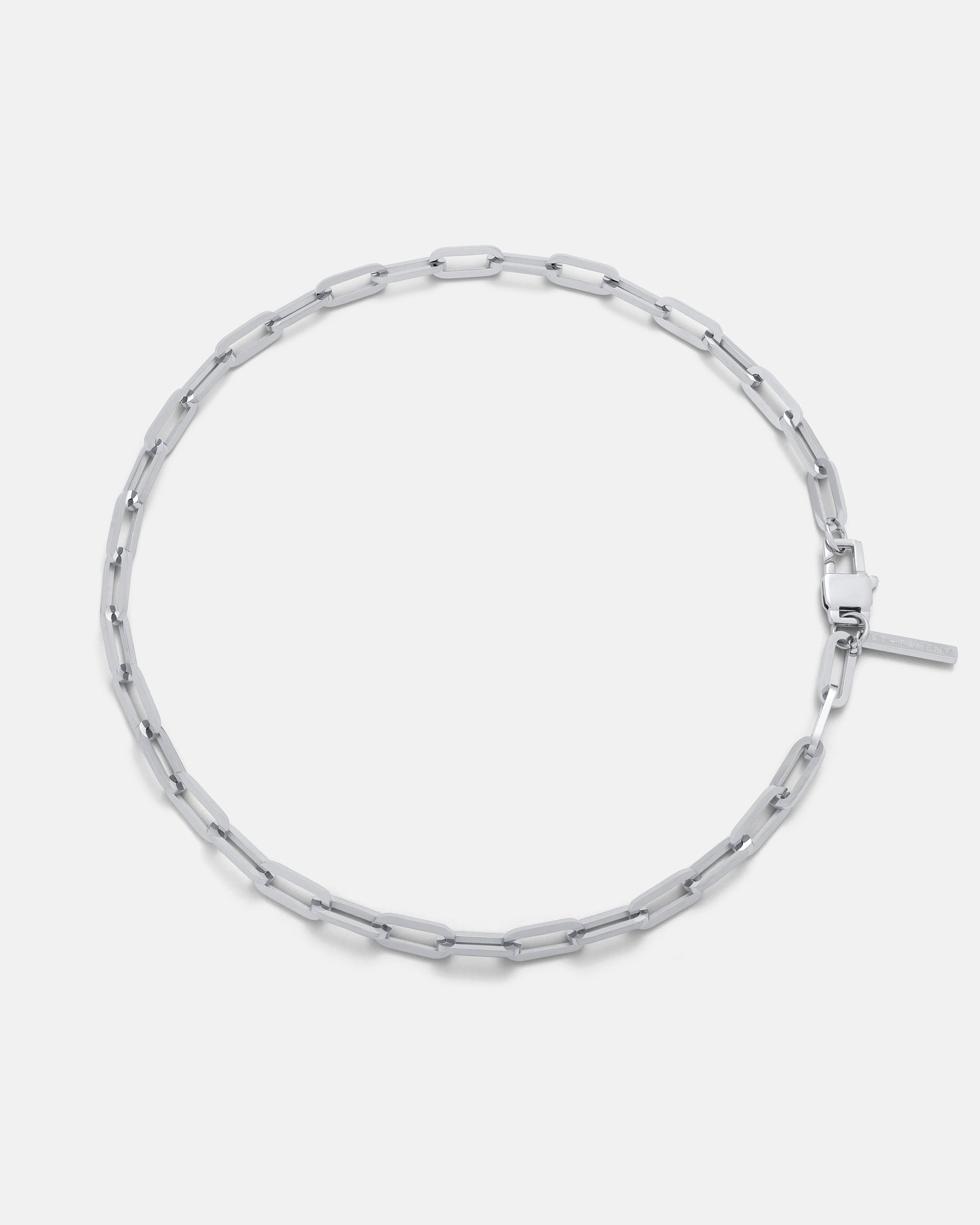 The Paperclip Chain is a silver necklace with elongated rectangular links and a simple clasp, shown in a circular shape on a white background—an ideal men’s accessory featuring an adjustable chain for the perfect fit.