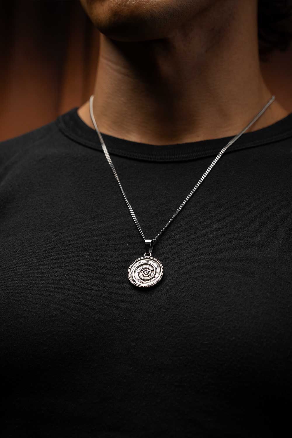Silver necklace with a pendant worn by a person on a black shirt