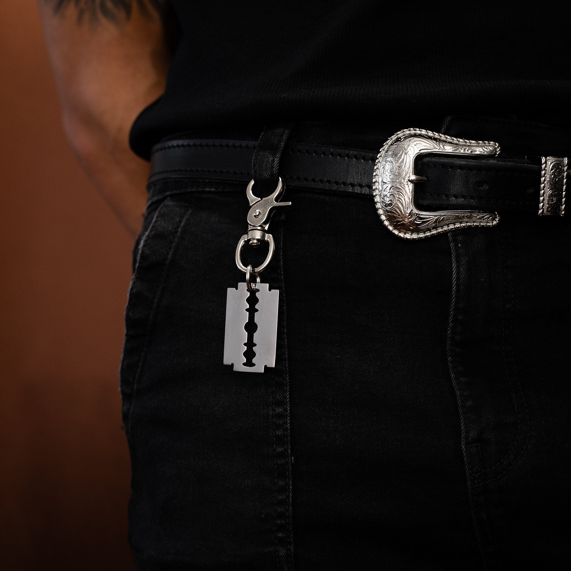Person wearing black pants with a silver belt and razorblade keychain on a brown background