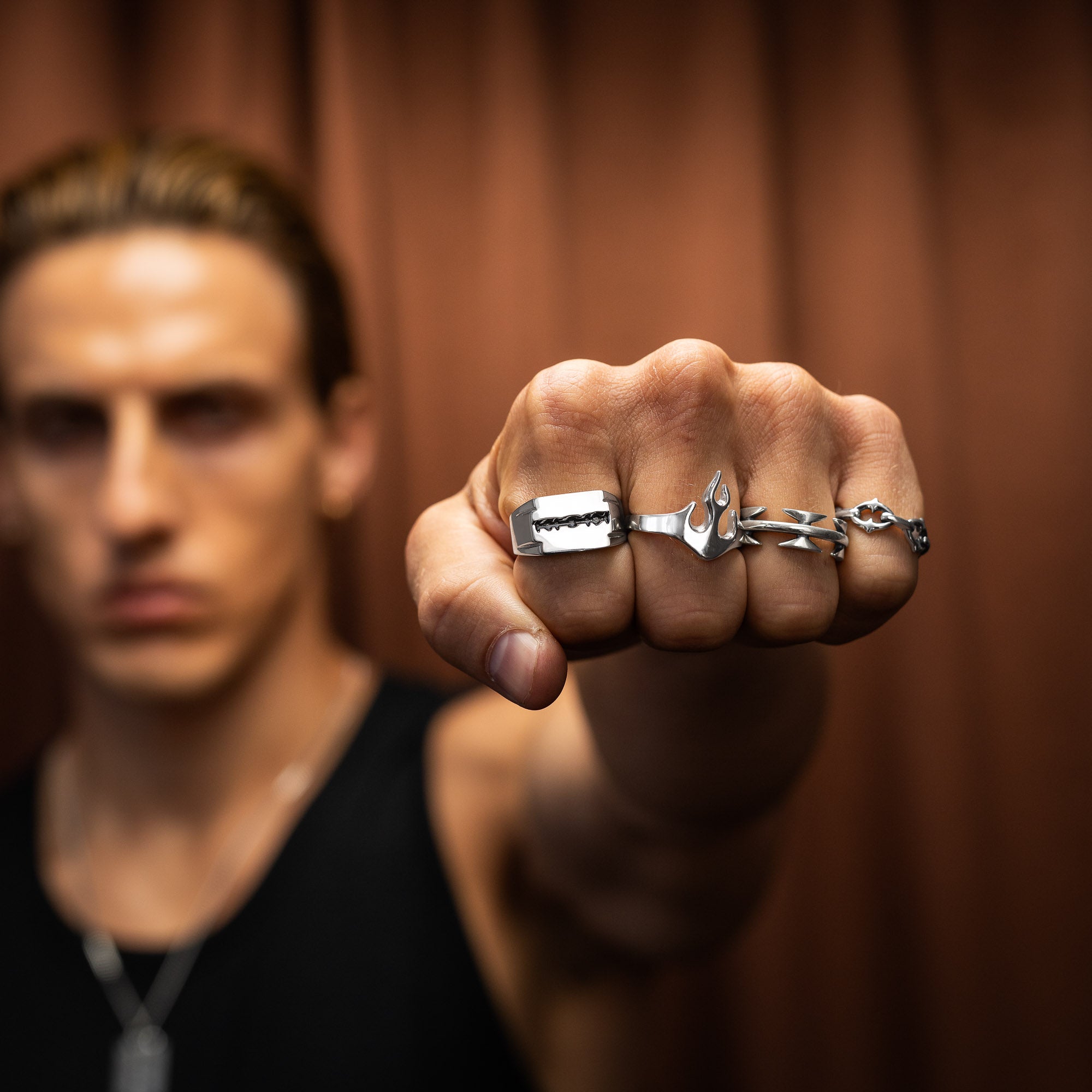 Man wearing a unique silver ring with a razorblade design on a brown background