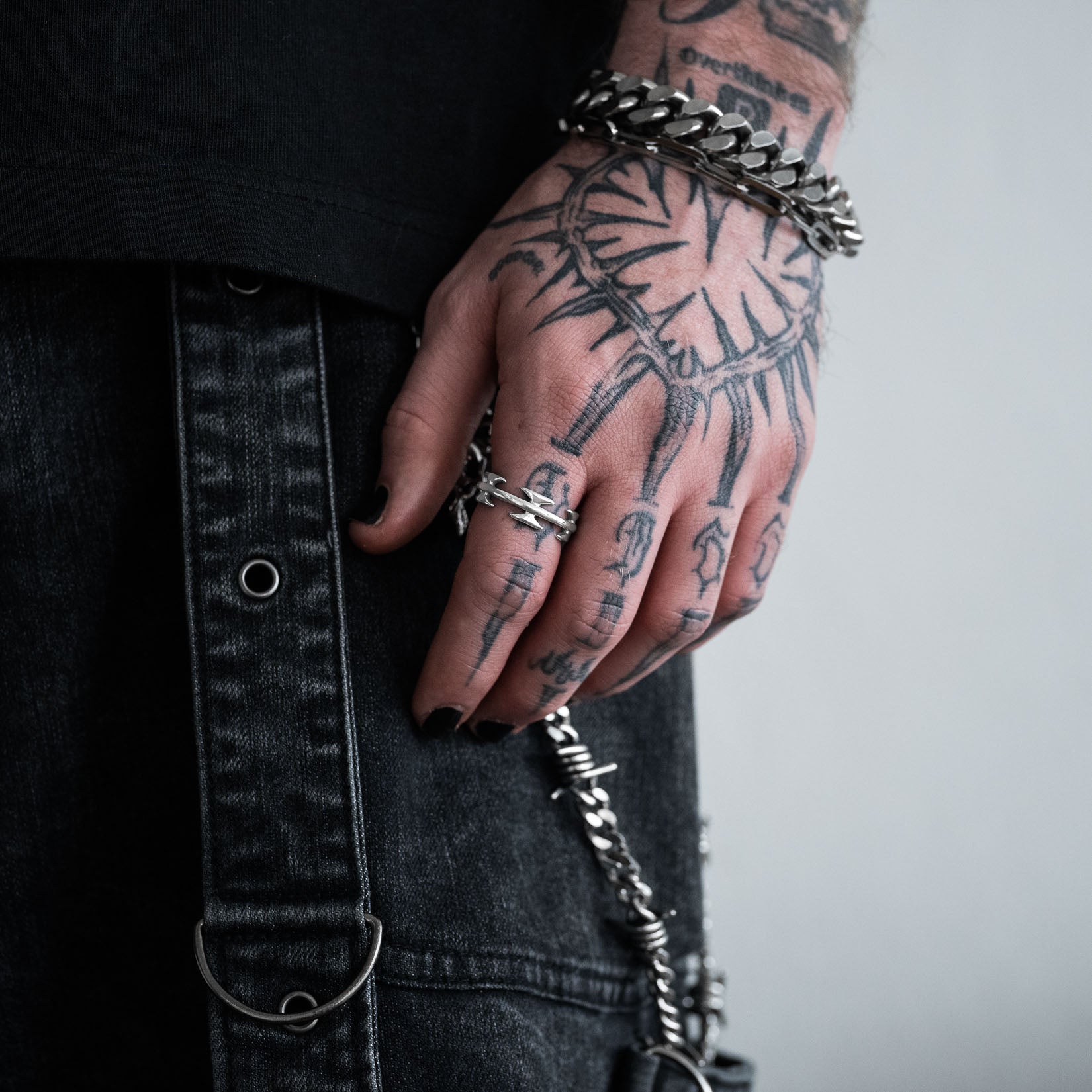 Hand with tattoos wearing a silver razorwire ring, against a neutral background. By statement collective