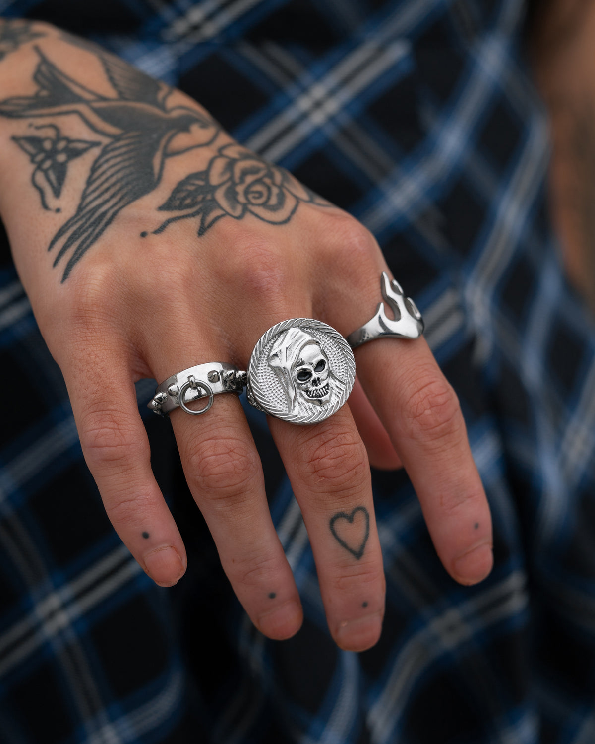 A hand wearing three silver rings: a circular The Reaper Sovereign Ring, a band with a small ring attachment, and a flame-shaped sovereign ring.