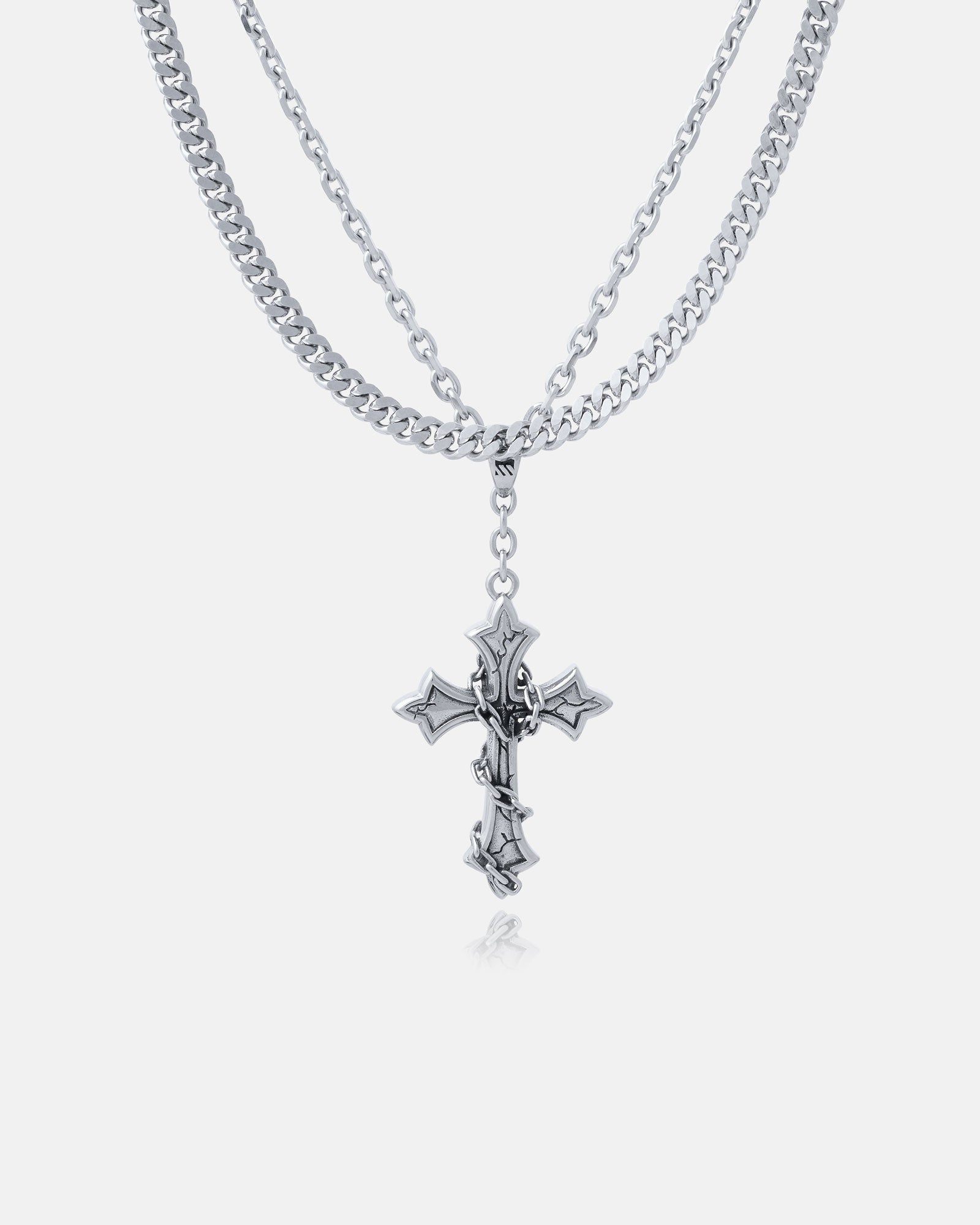 The Ruins" 6mm Set features a layered stainless steel necklace with a gothic cross pendant on the shorter chain and a Cuban link chain, all showcased against a plain white background.