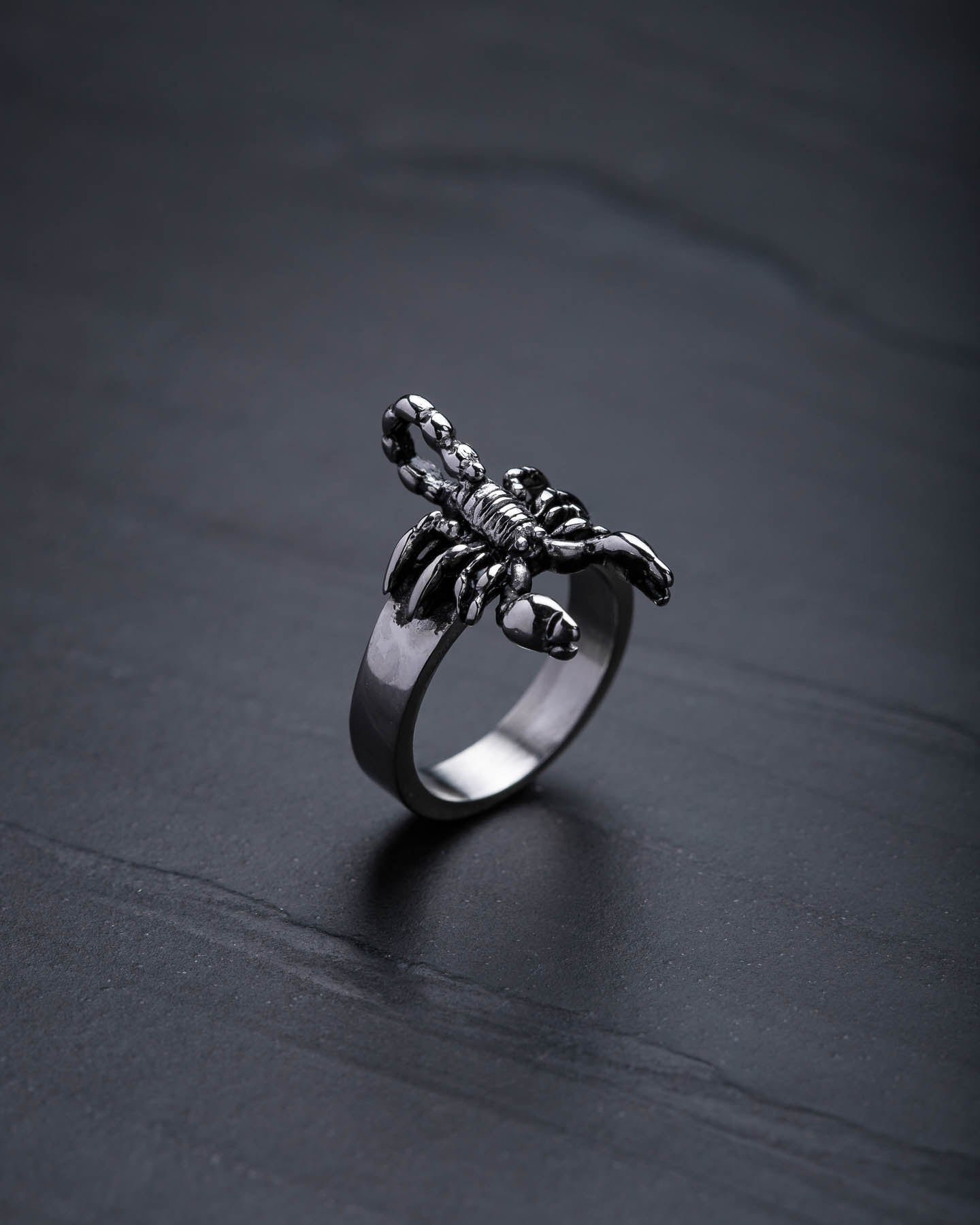 The Scorpion Ring features a detailed design and stands upright on a dark, textured surface—an eye-catching piece for scorpion jewelry lovers.