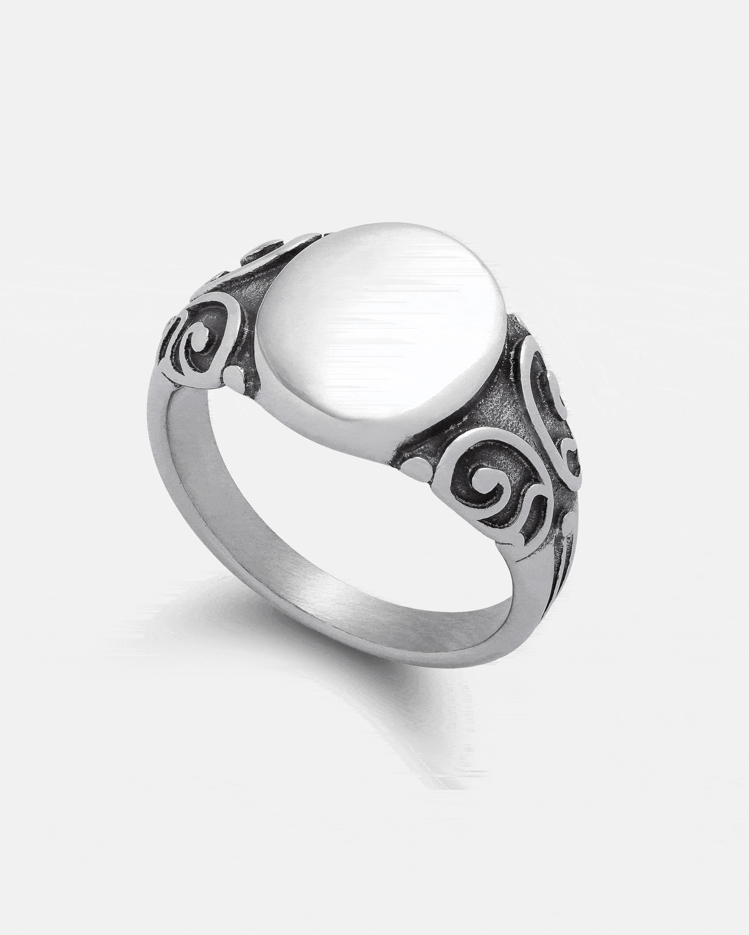 The Statement Collective Mini Oval Scroll Signet Ring features a plain, miniature oval signet centerpiece crafted from 316L stainless steel, with ornate traditional scrollwork engraving on both sides of the band, shown against a white background.