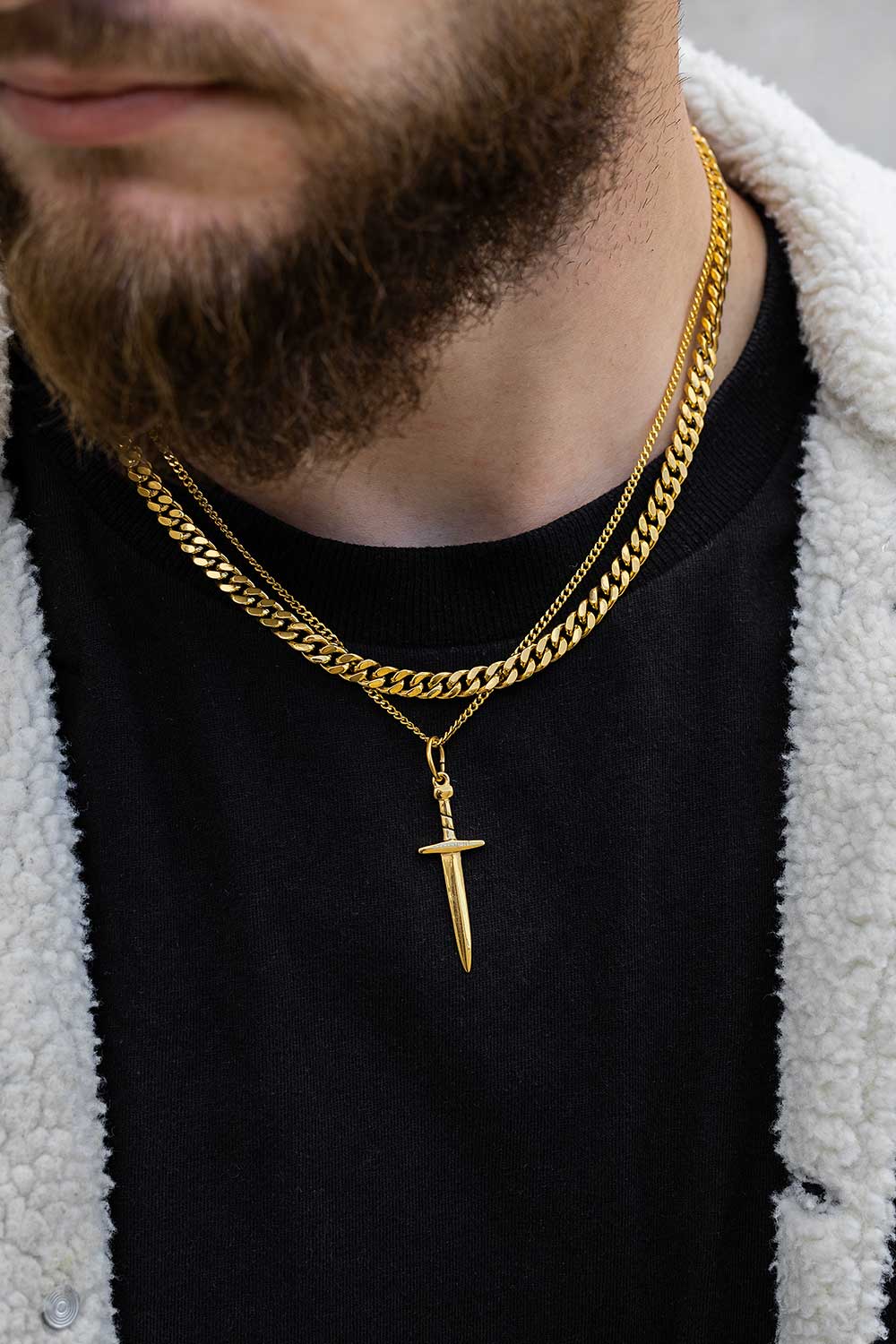 Man wearing a gold chain necklace with a dagger pendant.