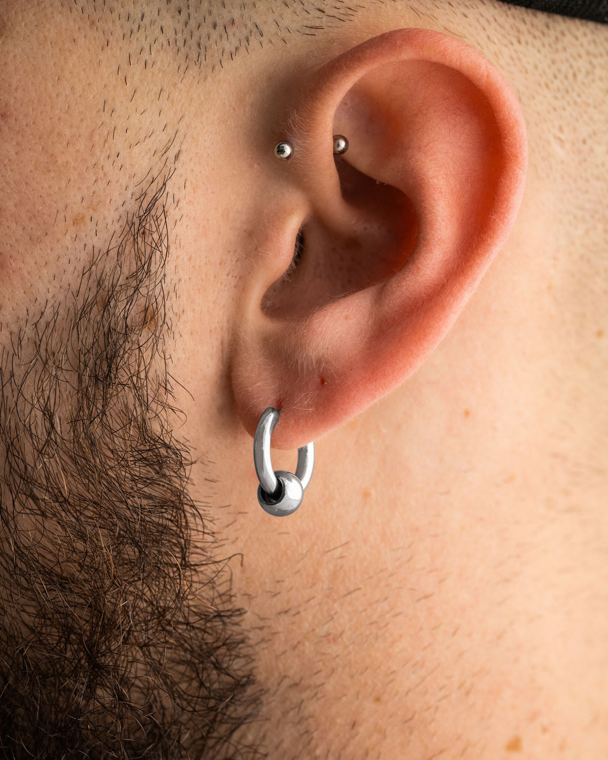 Statement Collective Ball Hoop Earrings worn in a pierced earlobe, with a small silver barbell piercing in the upper cartilage.