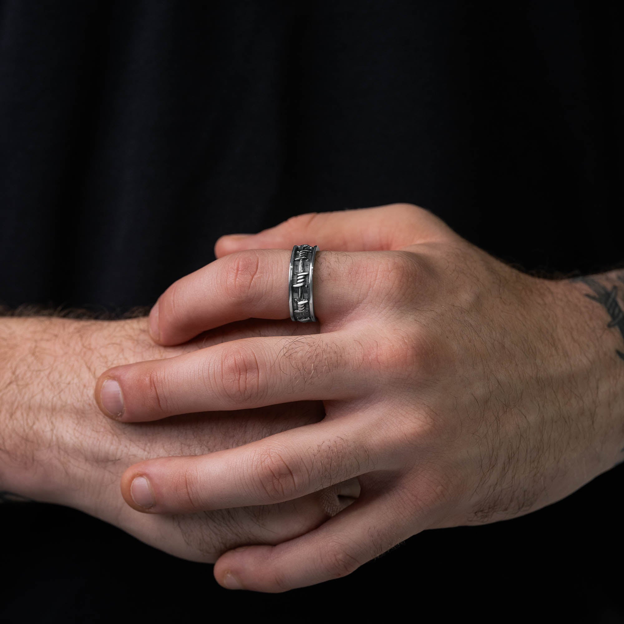 Silver ring with barbed wire details around entire ring, on male hand