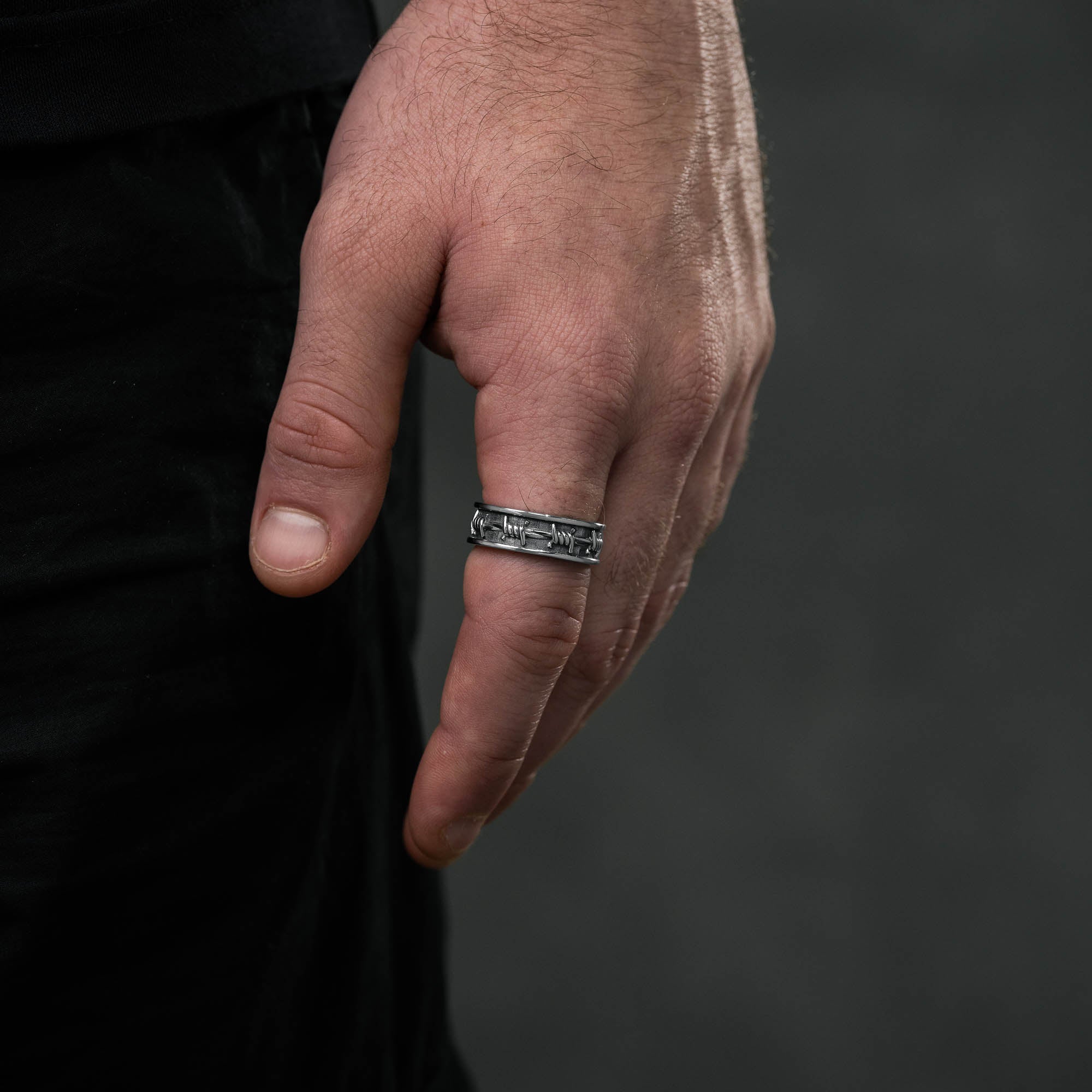 Silver ring with barbed wire details around entire ring, on male hand