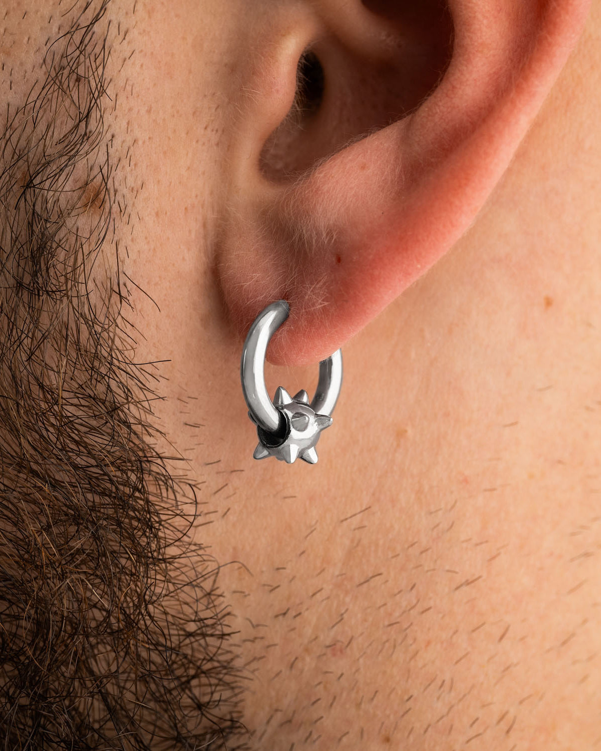 A silver Morning Star earring from Statement Collective featuring a small, spiked charm worn in a pierced earlobe.