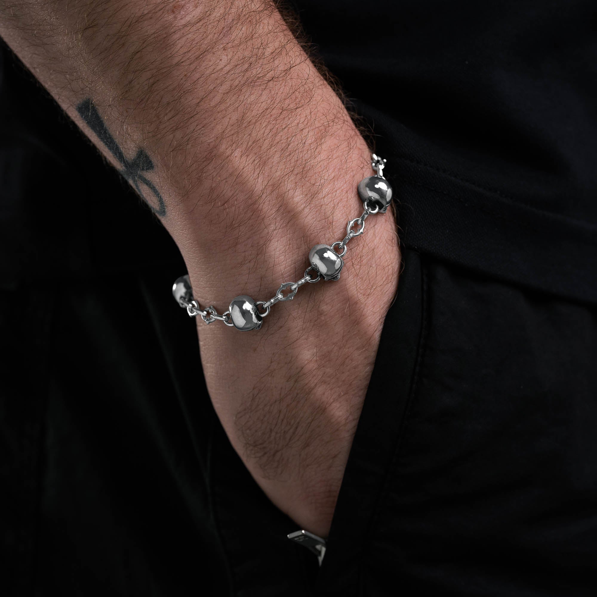 Silver spiked link bracelet with skull links all the way around on male model