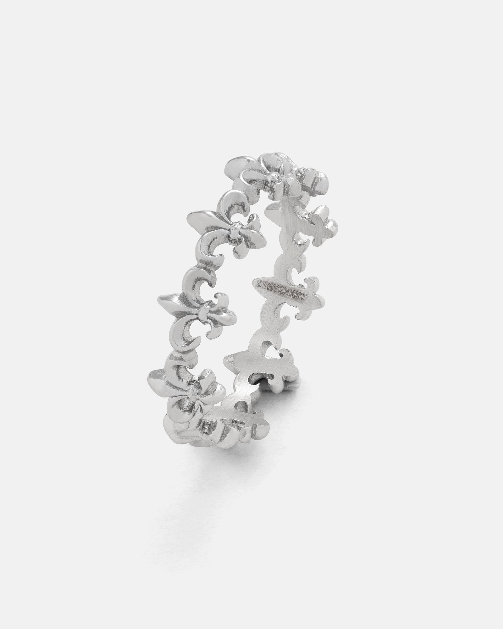 The “Fleur De Lis” Ring by Statement Collective showcases a repeating pattern of upright fleur-de-lis shapes in silver, displayed against a plain white background—ideal for stacking and versatile styling.
