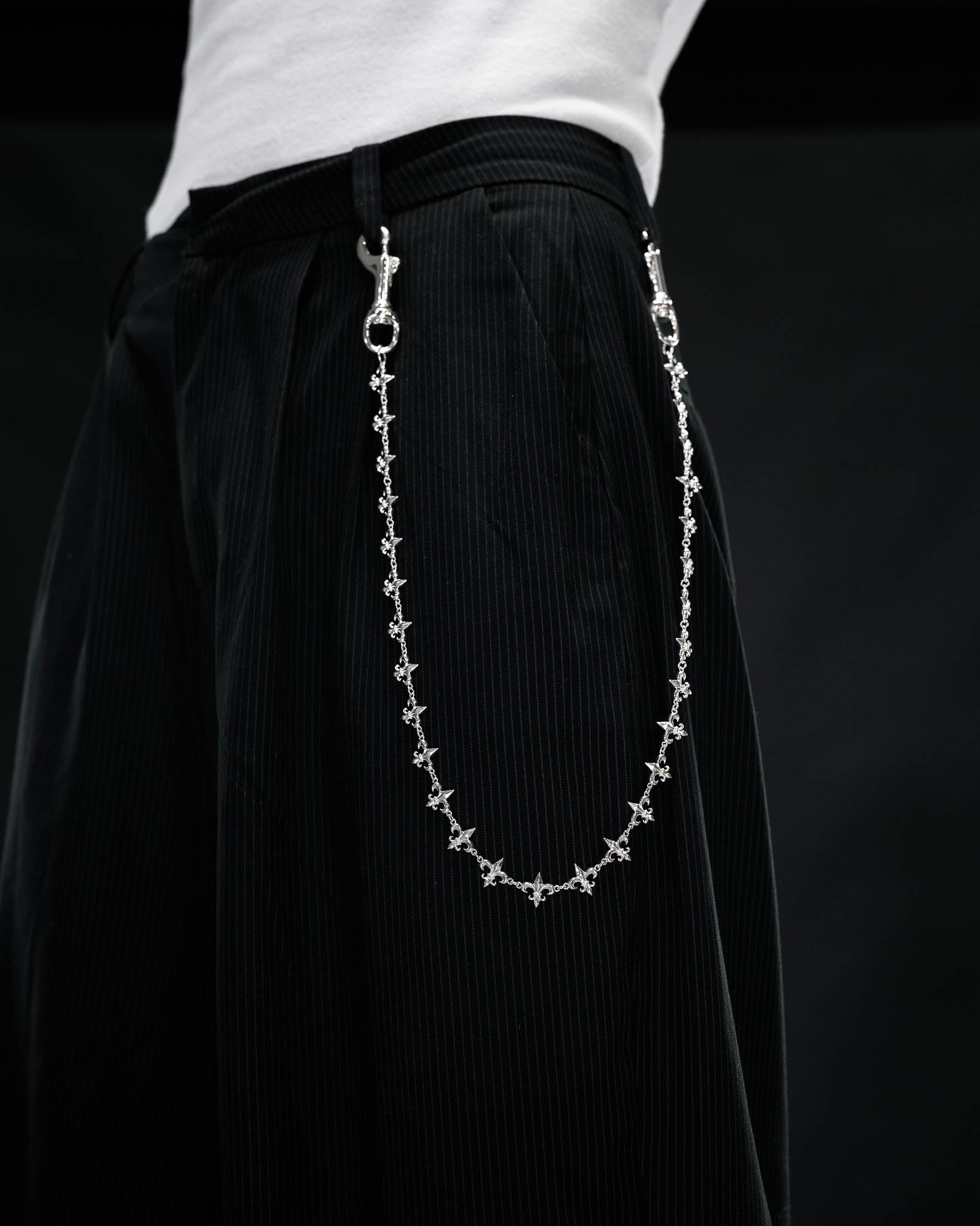 A person wearing black pinstripe pants with the Statement Collective “Fleur De Lis” Wallet Chain attached to the belt loops, photographed against a dark background.