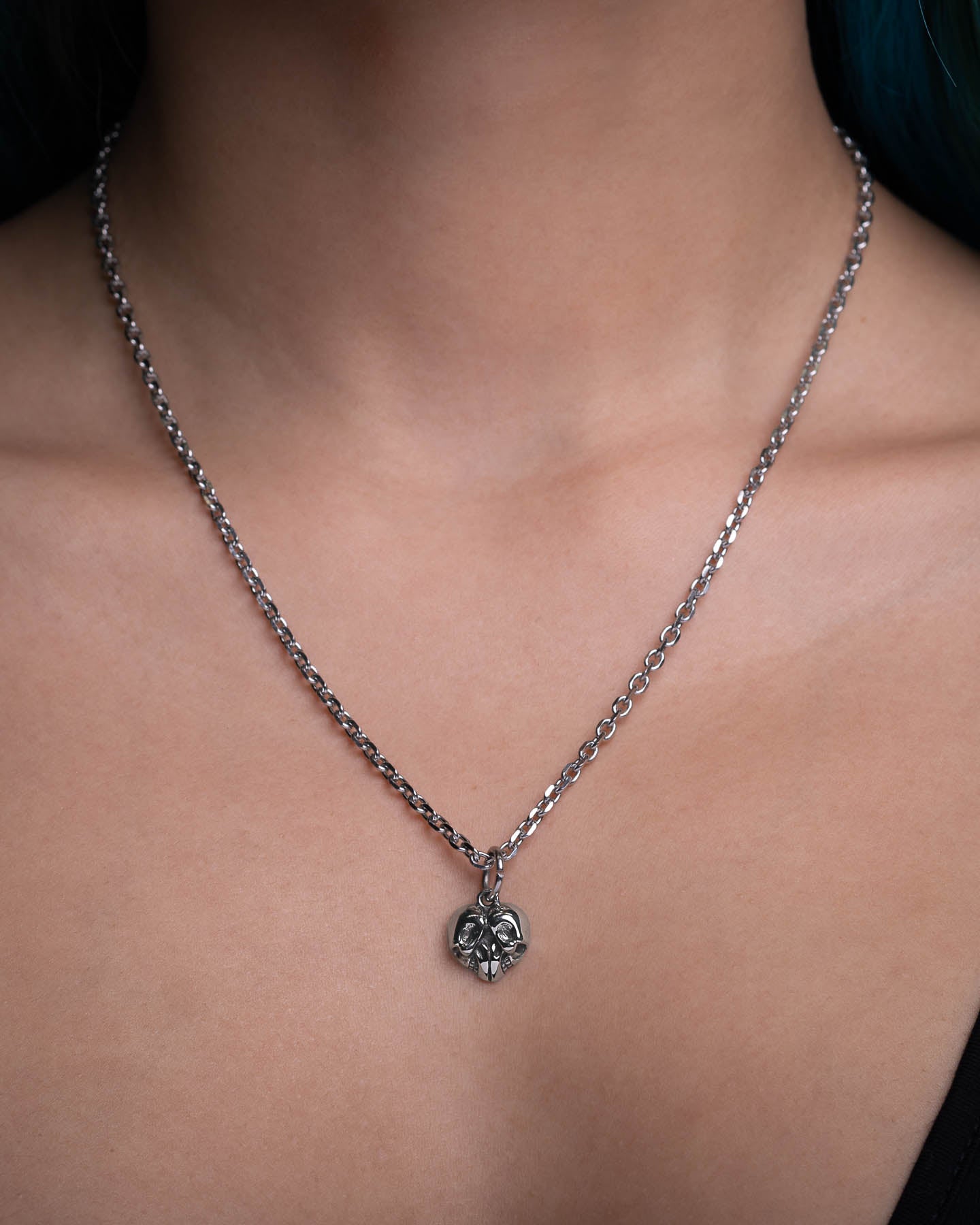 A close-up of a person wearing a stainless steel Skull Heart Pendant necklace against bare skin and a black top—a striking piece ideal for fans of dark romance jewelry.